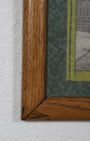 Corner of wood frame with small section of green mat and an unidentifiable portion of one photo showing