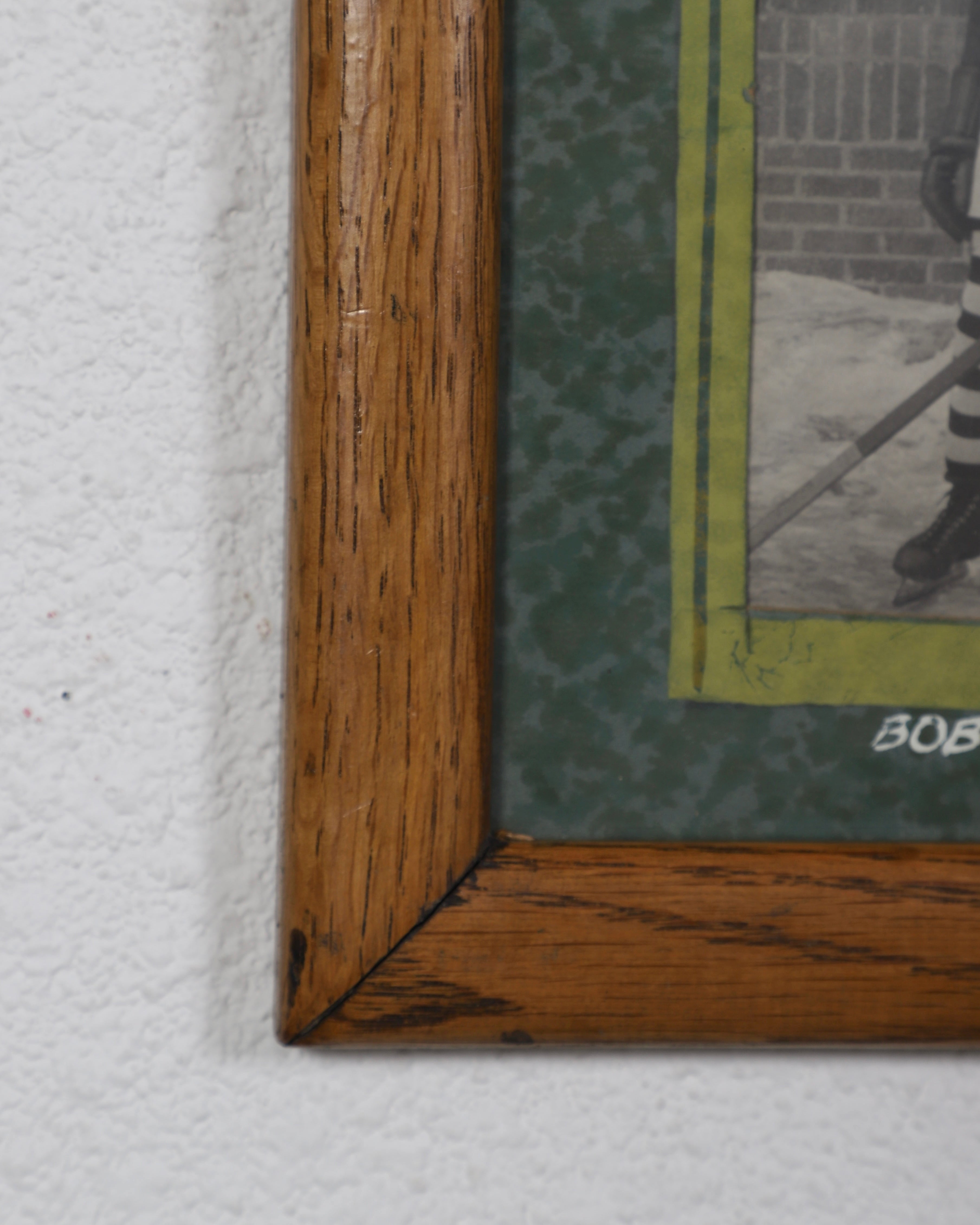 Corner of wood frame with small section of green mat and an unidentifiable portion of one photo showing