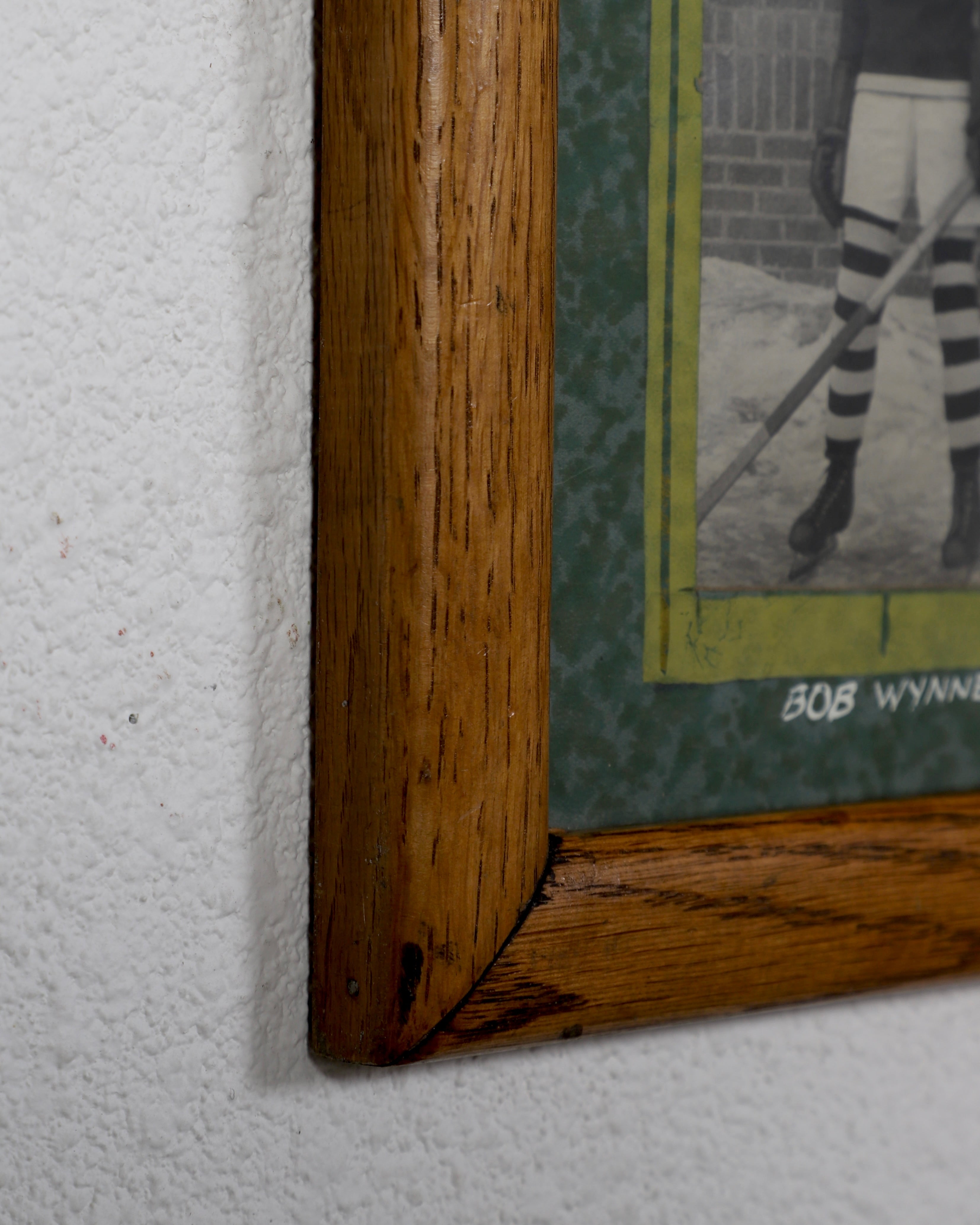 Corner of wood frame with small section of green mat and an unidentifiable portion of one photo showing