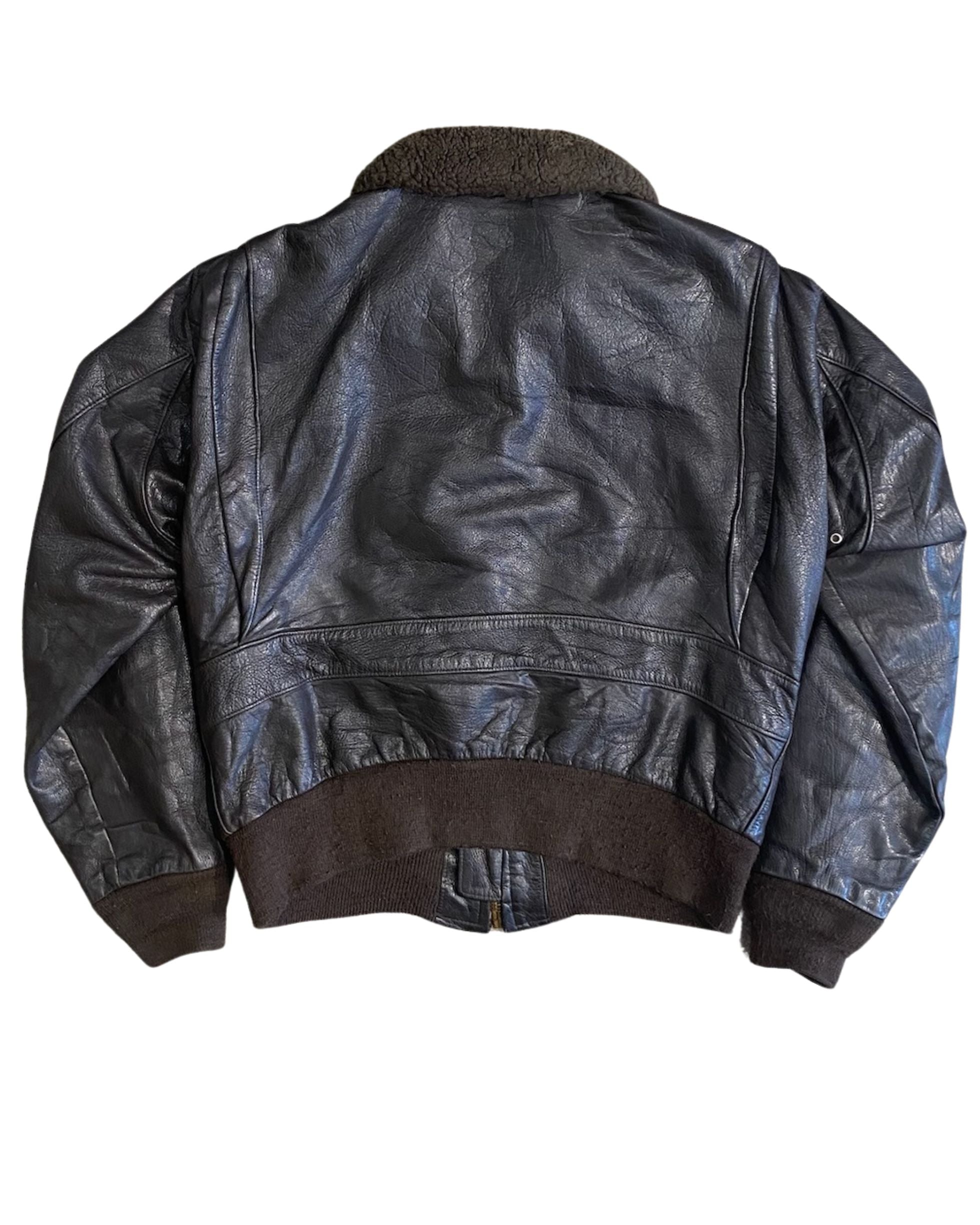 Back view of 1964 Schott Bros. USN G-1 flight jacket in dark seal brown leather with shearling collar, knit waistband, and back panel seam, on white background.