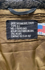 Front view of 1964 Schott Bros. USN G-1 flight jacket showing brass zip, snap-flap chest pockets with Schott S snaps, shearling collar, and knit cuffs, on white background.