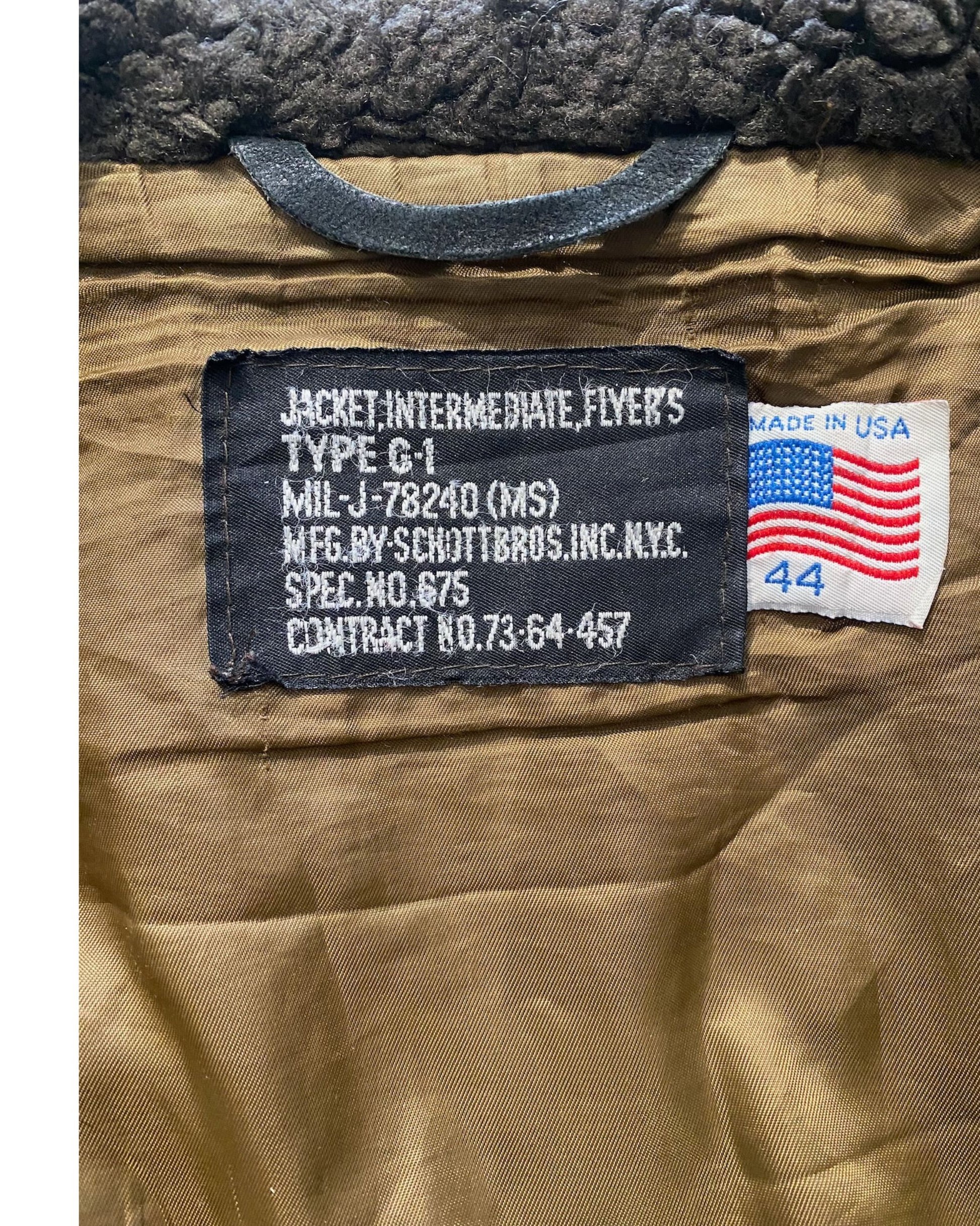 Front view of 1964 Schott Bros. USN G-1 flight jacket showing brass zip, snap-flap chest pockets with Schott S snaps, shearling collar, and knit cuffs, on white background.