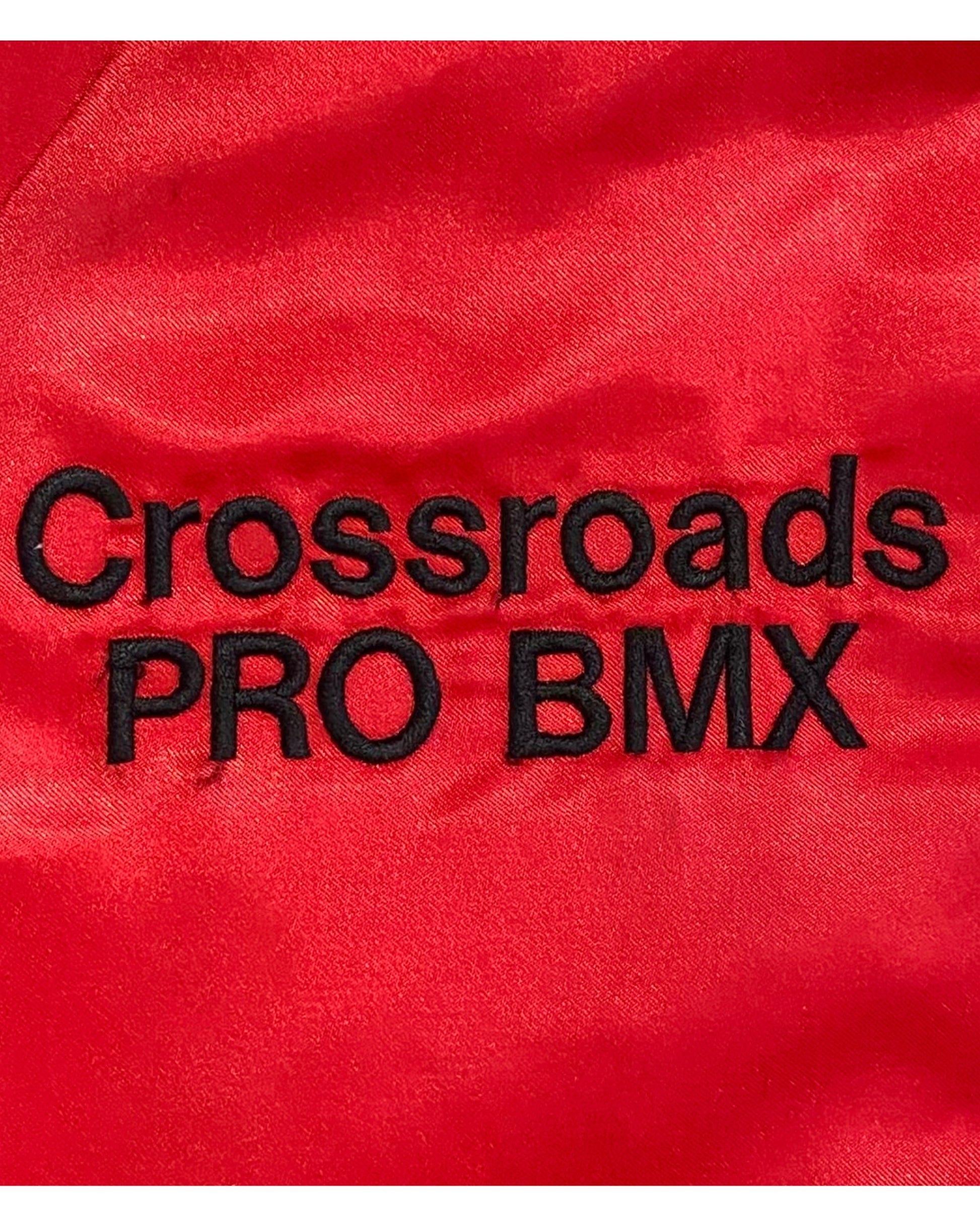 Close-up of a red satin or silk fabric with black embroidered text reading 'Crossroads PRO BMX'.