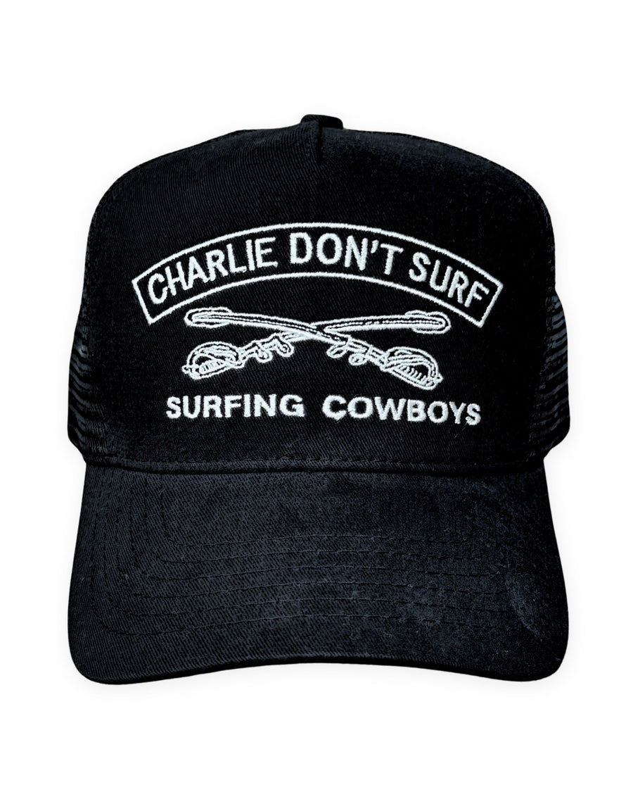Front view of Surfing Cowboys Charlie Don’t Surf trucker hat in black with white embroidery, mesh back, and adjustable snapback closure.