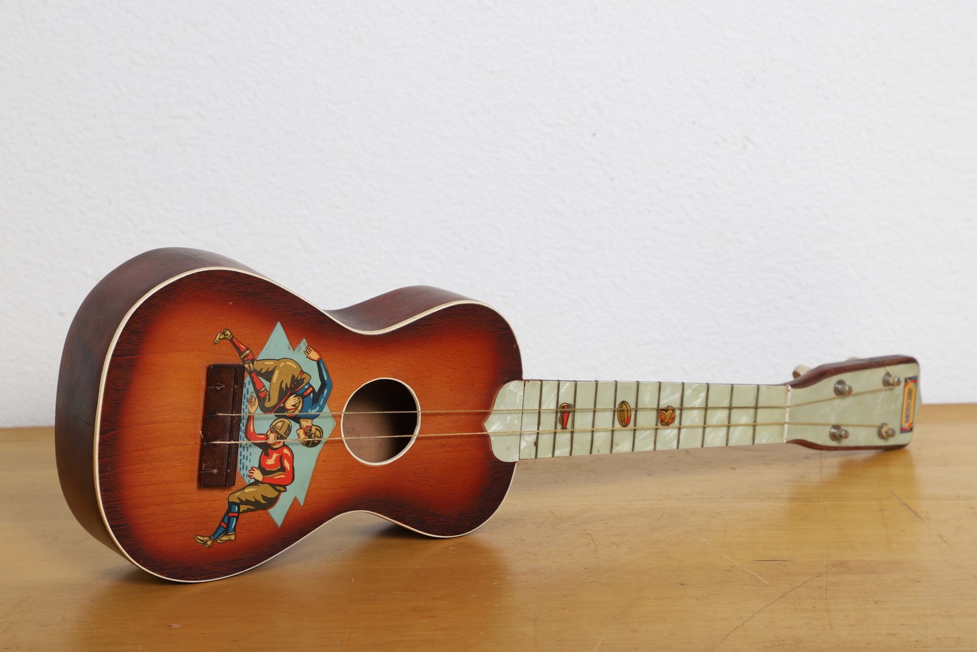  Vintage soprano ukulele with 1920s football scene graphic on body.