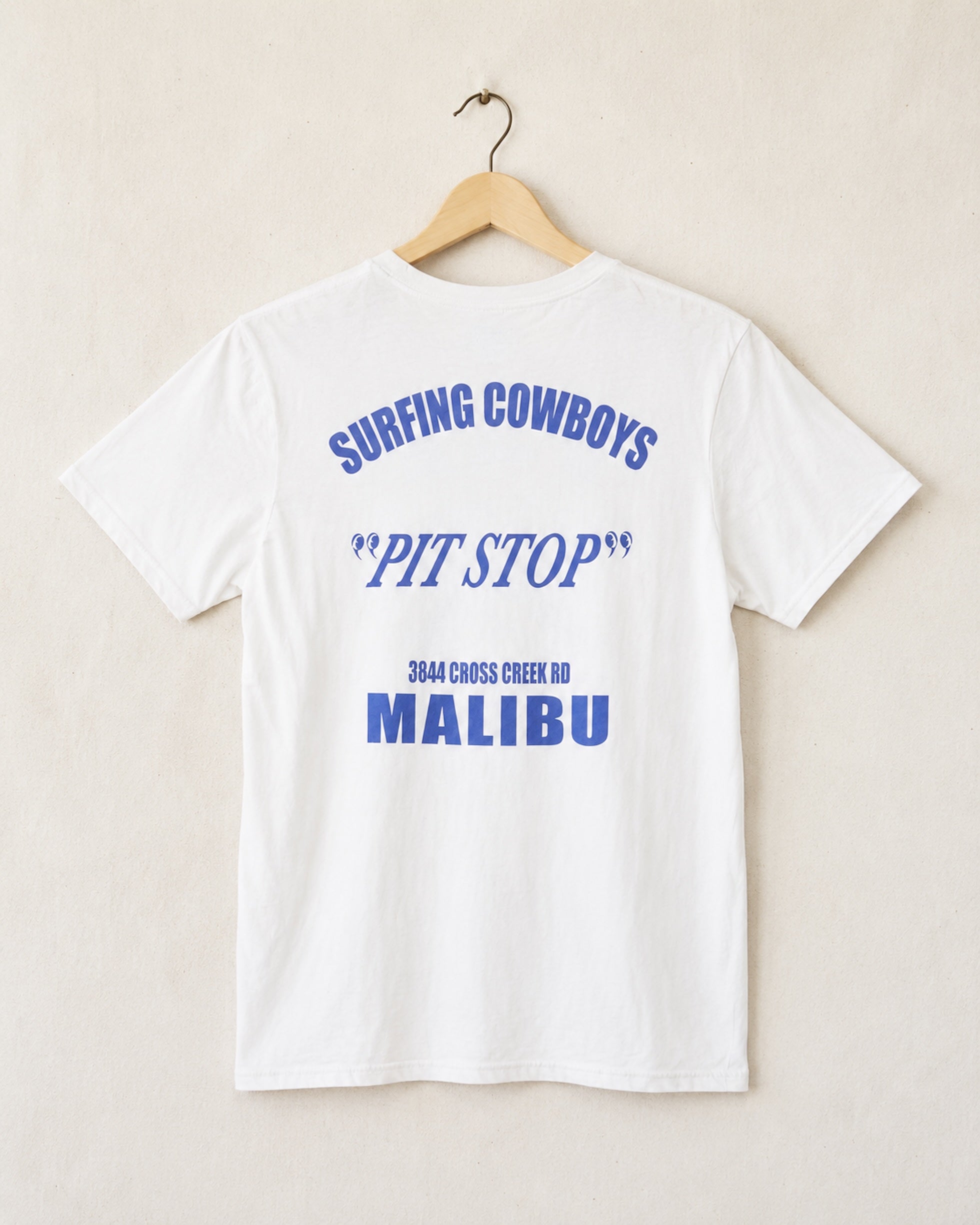Back of white t-shirt with blue graphic writing - shirt is hanging in front of a light beige background.
