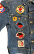 Close-up of the left front of a Lee denim jacket with “Skiers Are Better Lovers,” 1976 Blood Rally, Road Runners rally, and other vintage patches and pins.