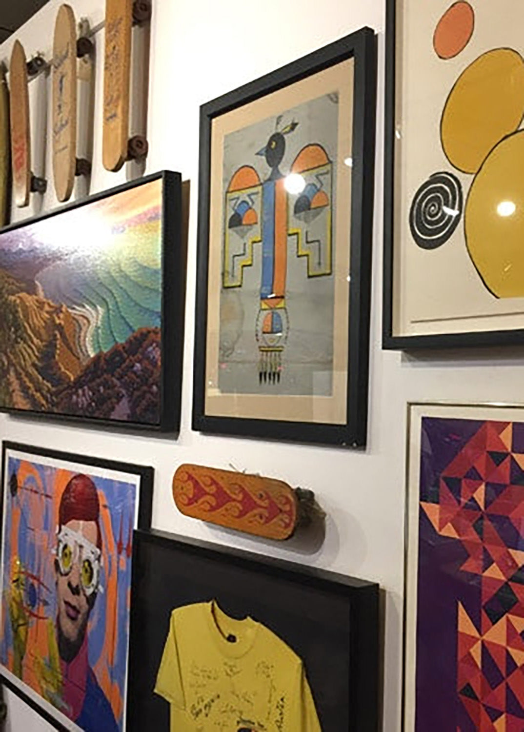 Wall with various framed artworks including abstract paintings and a skateboard