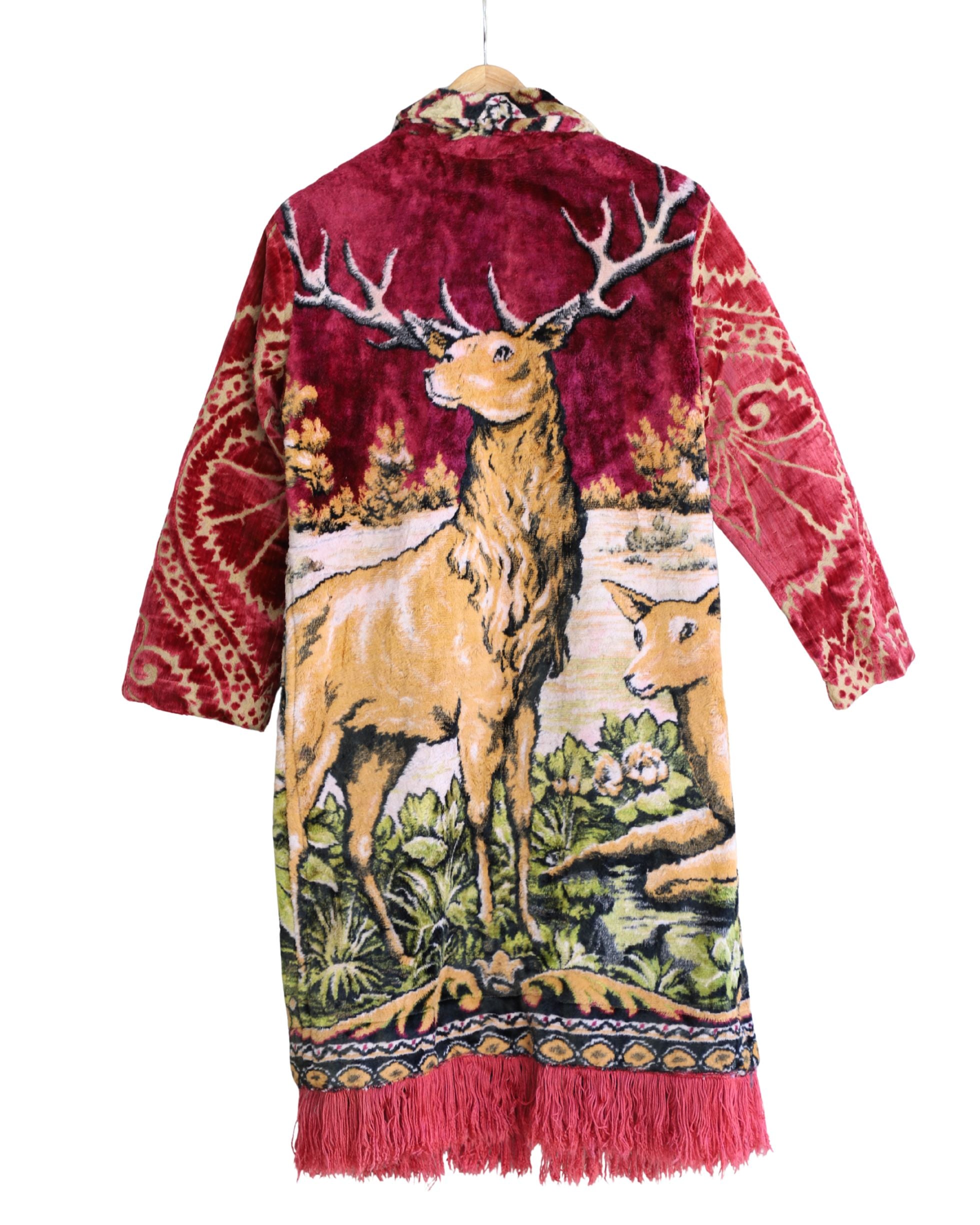 Artisan tapestry coat with stag and deer design, red velvet sleeves, and fringe hem. Handmade one-of-a-kind outerwear in vivid colors.
