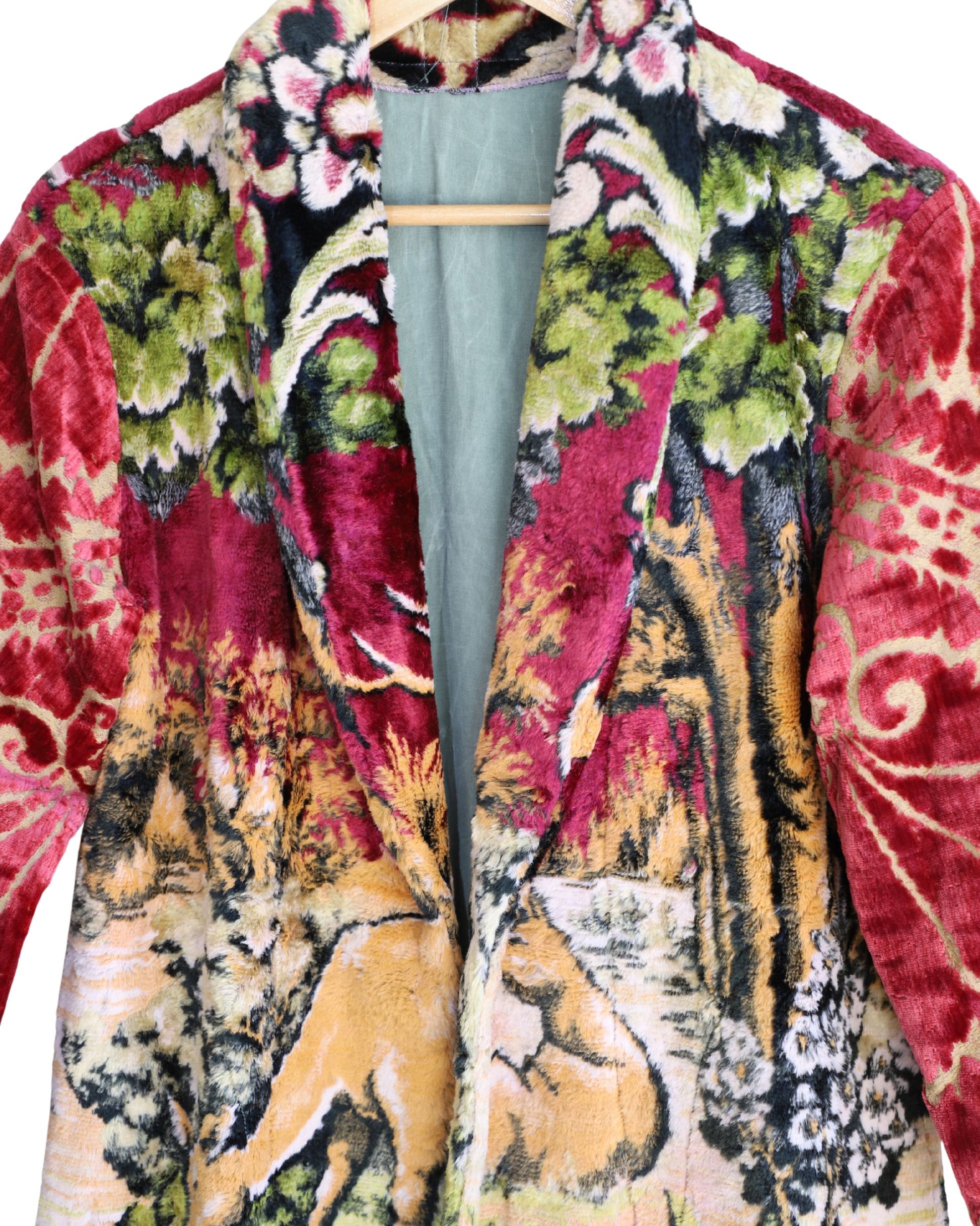 Artisan tapestry coat with stag and deer design, red velvet sleeves, and fringe hem. Handmade one-of-a-kind outerwear in vivid colors.