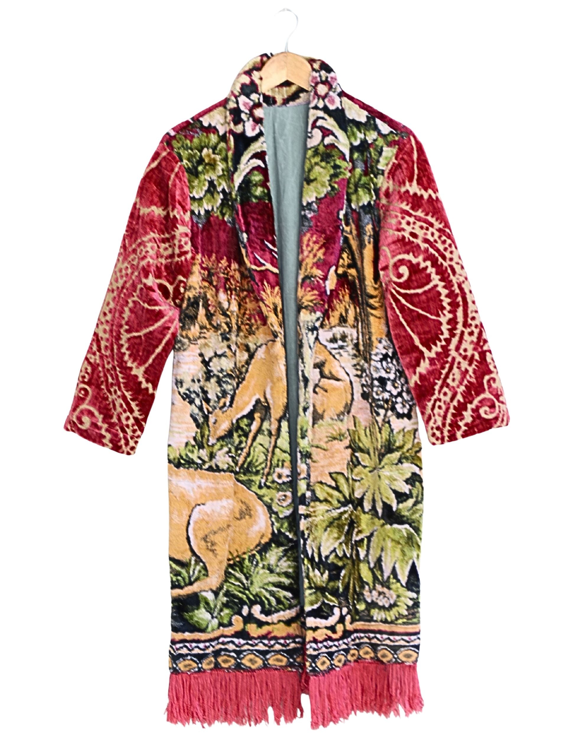 Artisan tapestry coat with stag and deer design, red velvet sleeves, and fringe hem. Handmade one-of-a-kind outerwear in vivid colors.