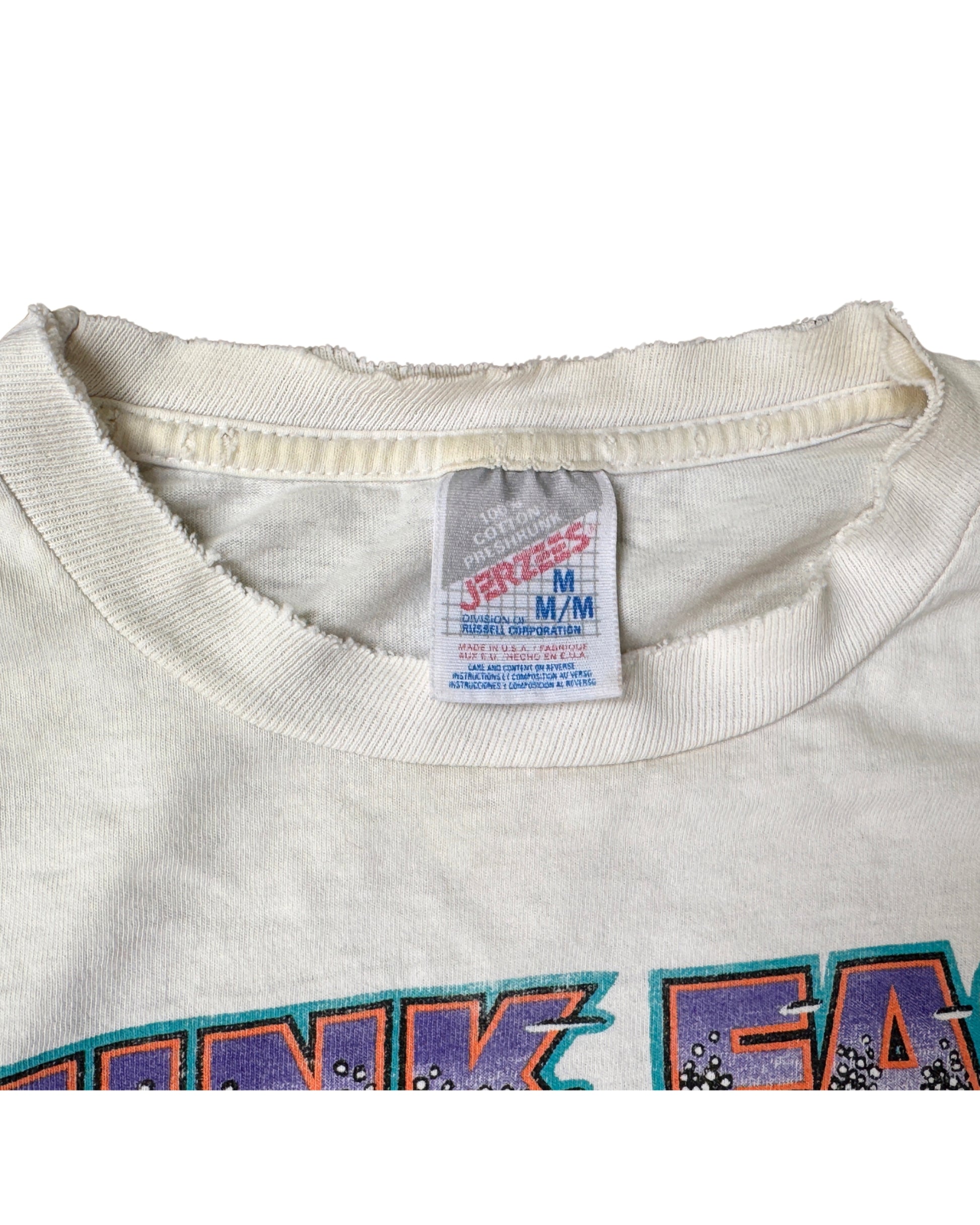 Close-up of the frayed ribbed neckline and Fruit of the Loom Medium label marked 100% cotton and Made in USA.
