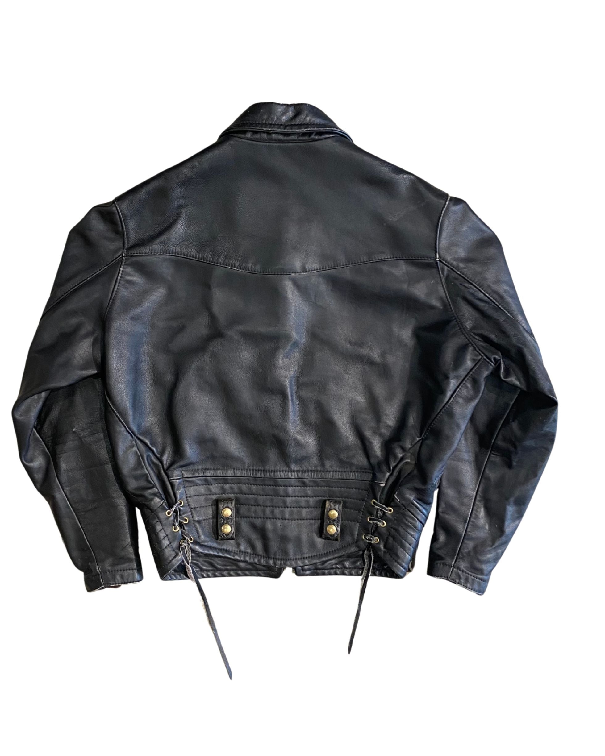 Back view of vintage 1970s black leather motorcycle jacket showing lace-up side adjusters, brass grommets, quilted waistband, on white background.