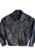 Front view of vintage 1970s black leather motorcycle jacket with brass center zip, angled zip pockets, circular chest medallion, and snap quilted collar, on white background.