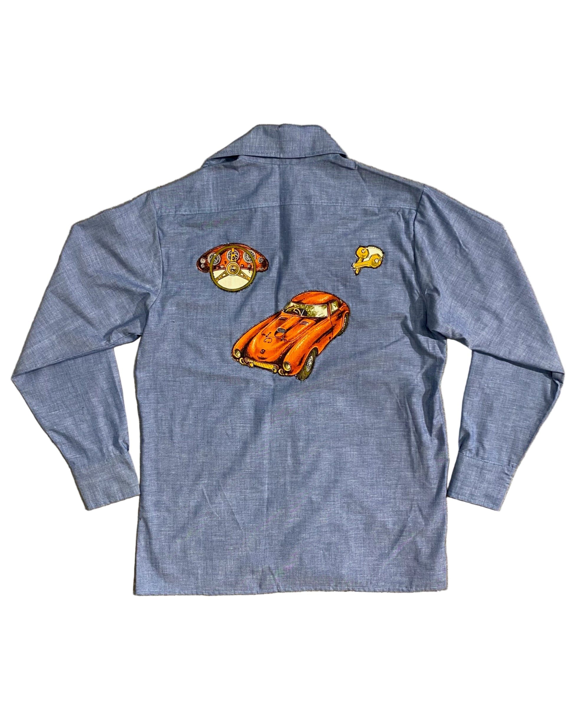 Back view of vintage 1980s chambray shirt featuring large orange sports car appliqué, steering wheel patch, and retro automotive accents.