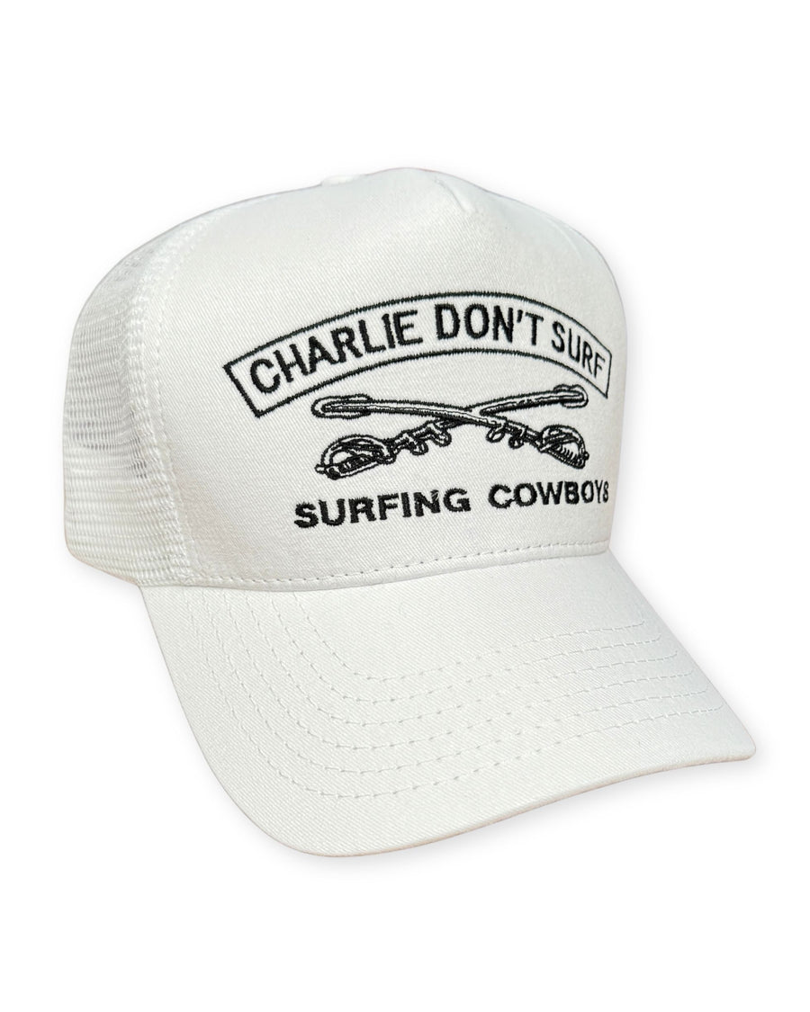 Surfing Cowboys Charlie Don’t Surf trucker hat in white with black embroidery, mesh back, and adjustable snapback closure.