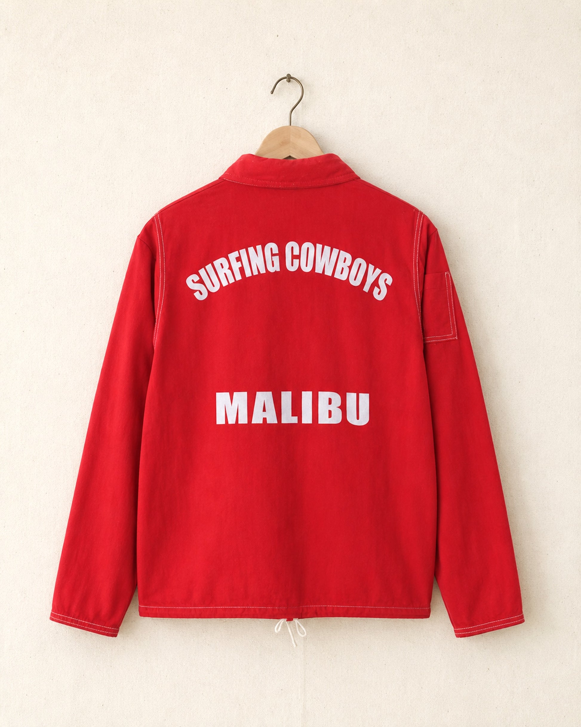 Red jacket with 'Surfing Cowboys Malibu' text on a beige background