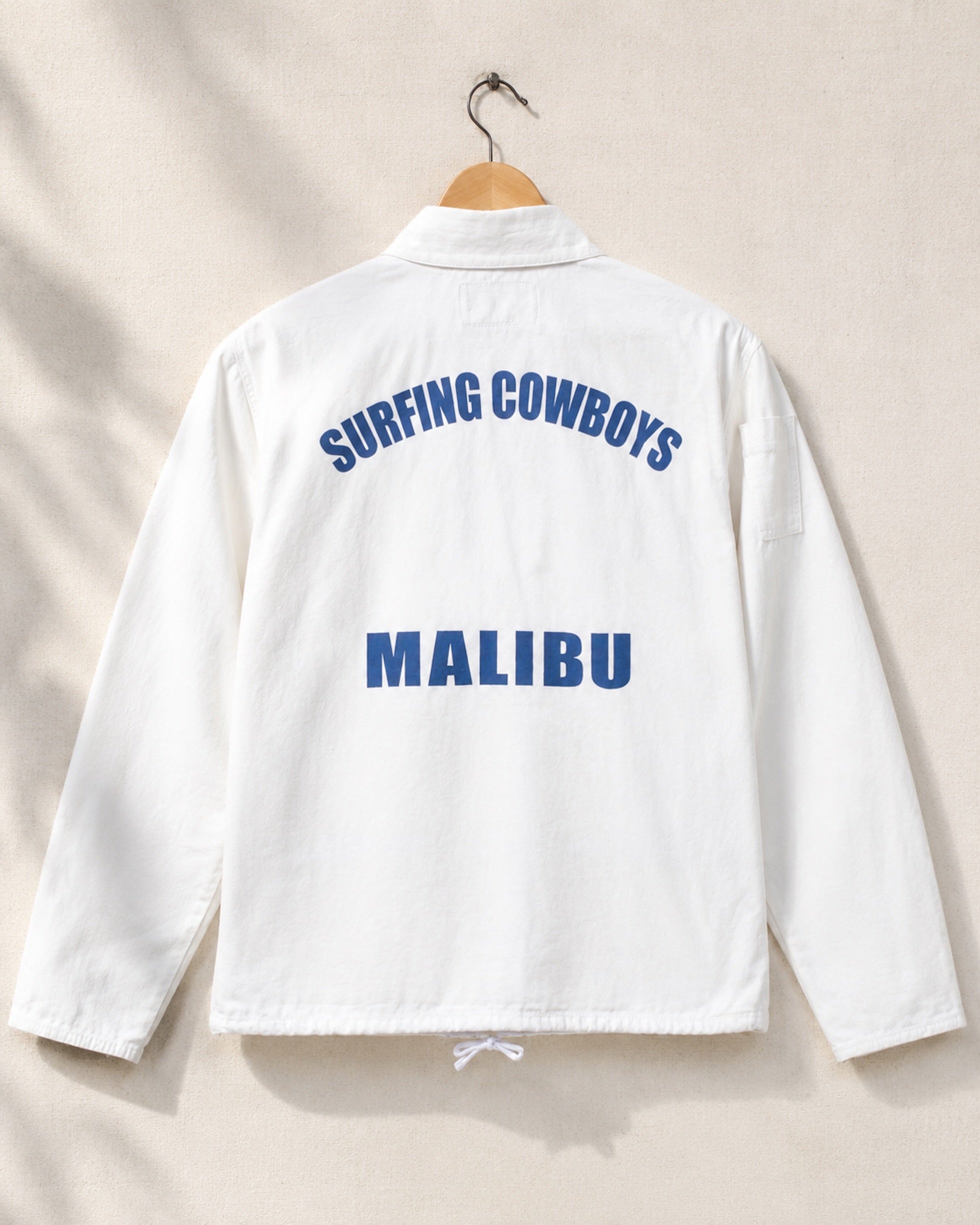 White jacket with 'Surfing Cowboys Malibu' text on a beige background