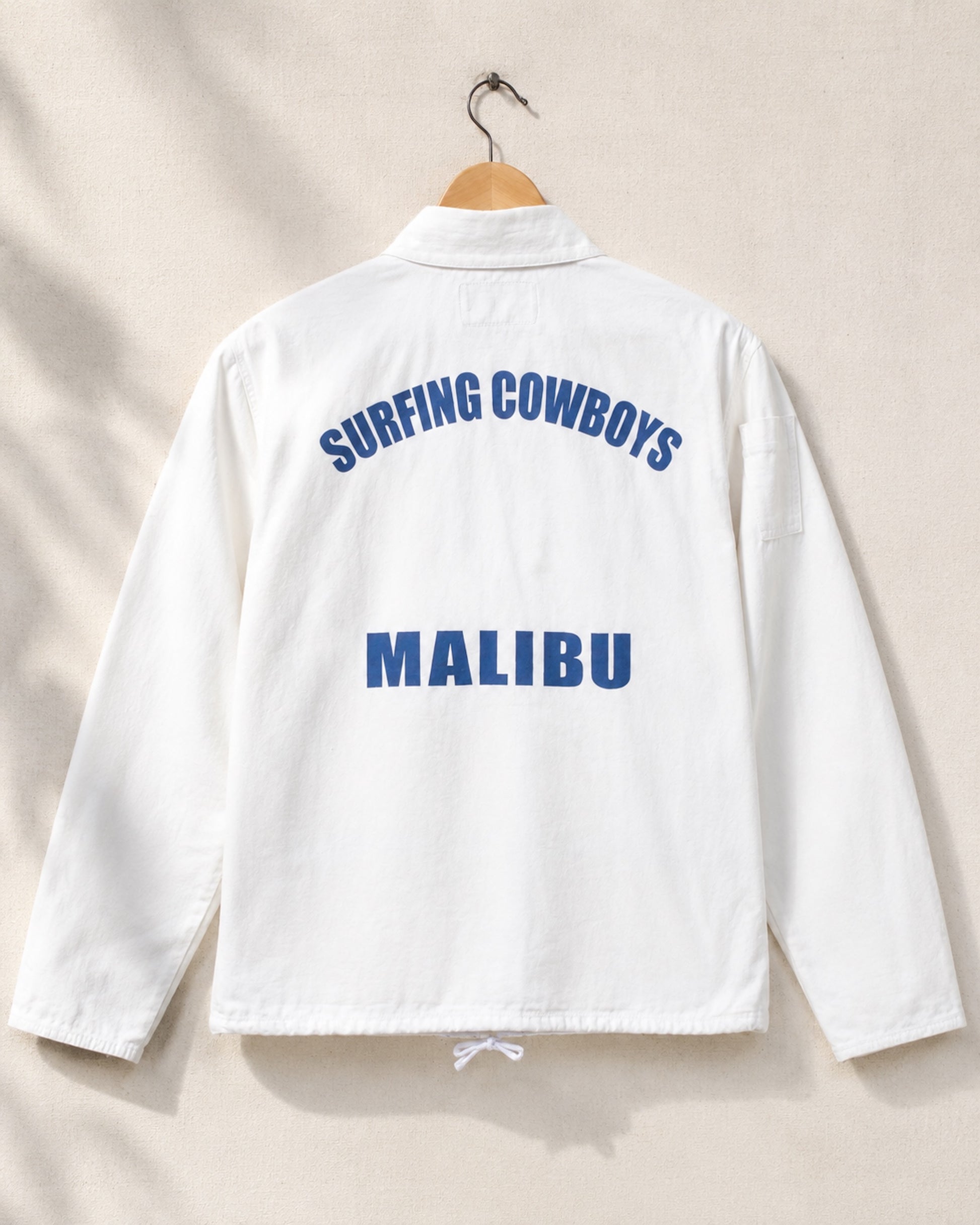 White jacket with 'Surfing Cowboys Malibu' text on a beige background