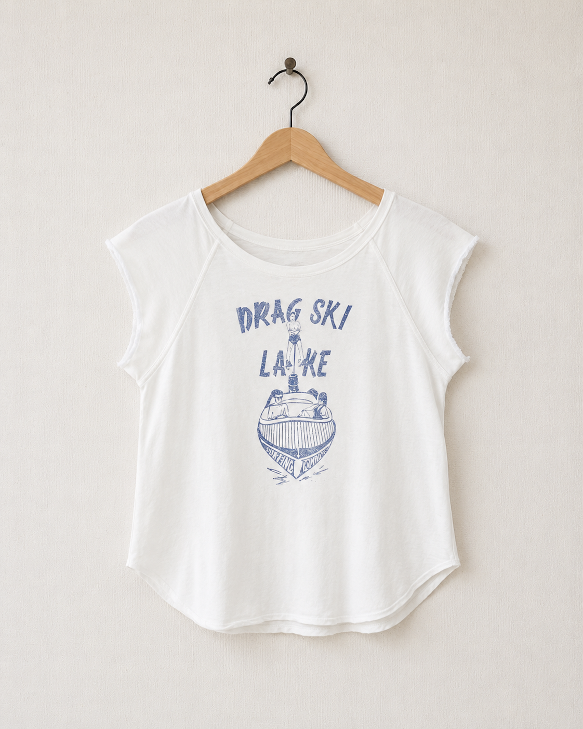 Front view of a vintage-white women’s raglan top with raw cap sleeves, a curved hem, and a faded blue Drag Ski Lake motorboat graphic.