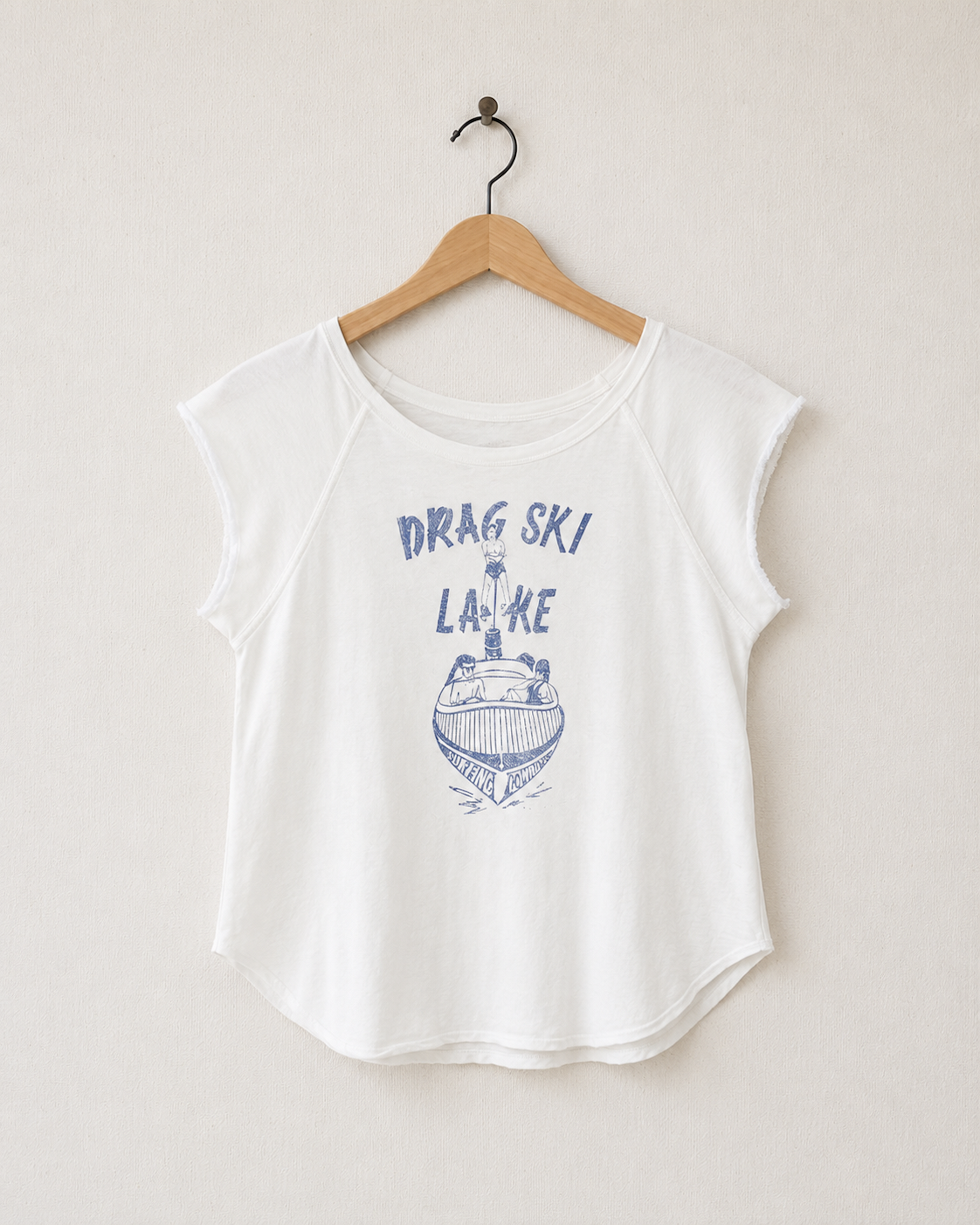Front view of a vintage-white women’s raglan top with raw cap sleeves, a curved hem, and a faded blue Drag Ski Lake motorboat graphic.