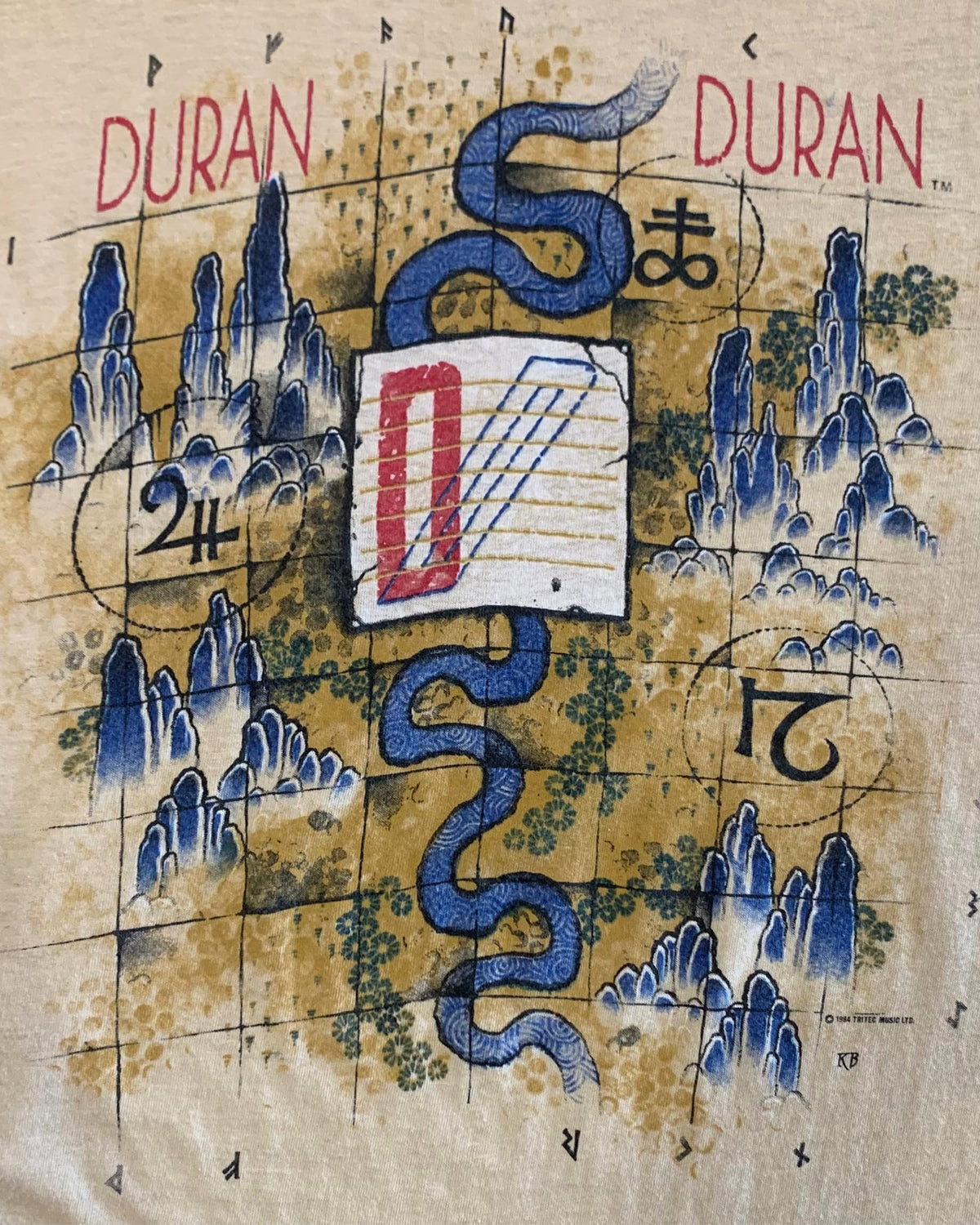 Close-up of the Duran Duran 1984 front graphic showing a blue serpent, stylized blue mountains, symbols, numbers, and ©1984 Tritec Music Ltd. marking.