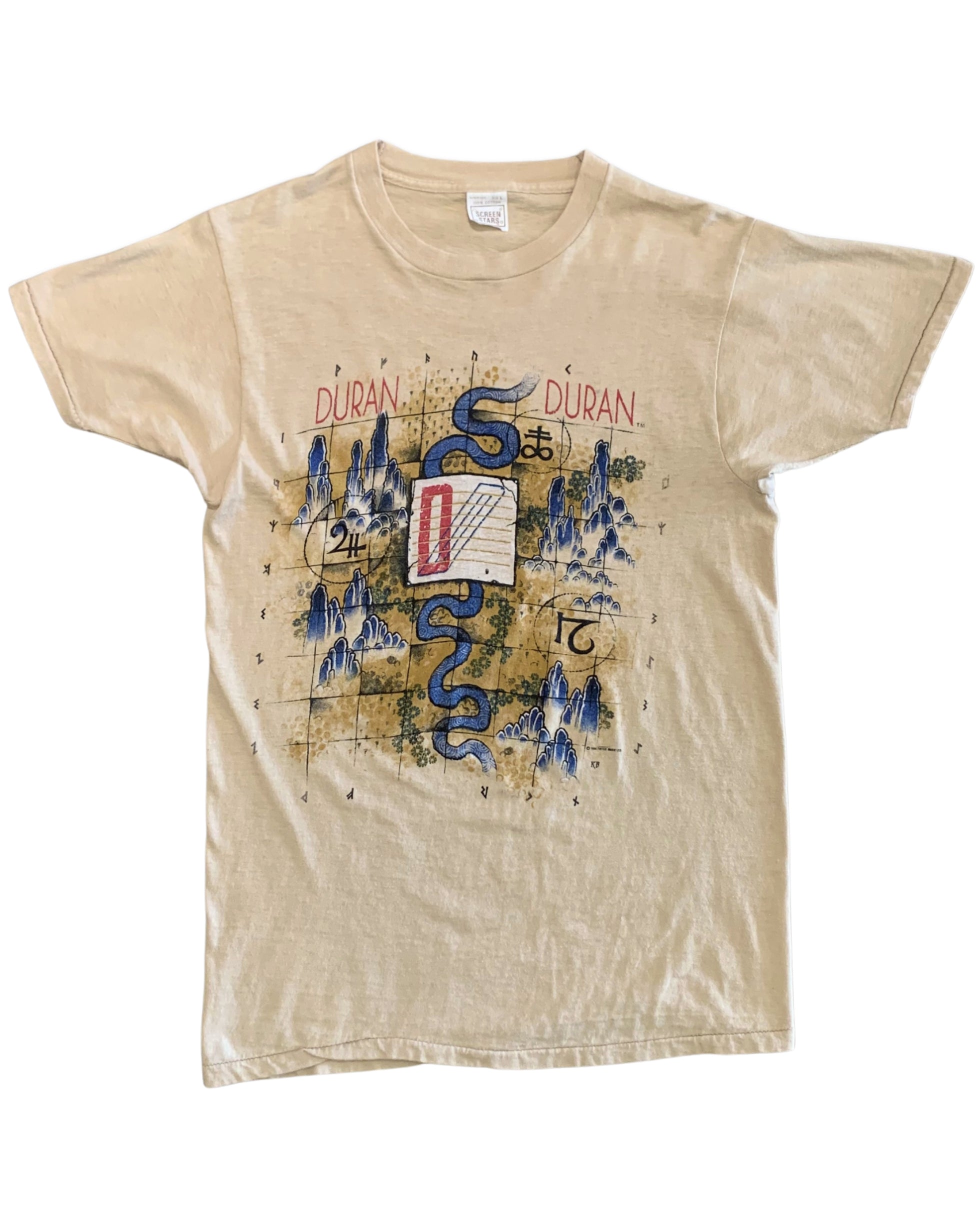 Front view of a beige Duran Duran 1984 tour T-shirt with a blue serpent, stylized mountains, numbers, symbols, and red and blue graphic details.
