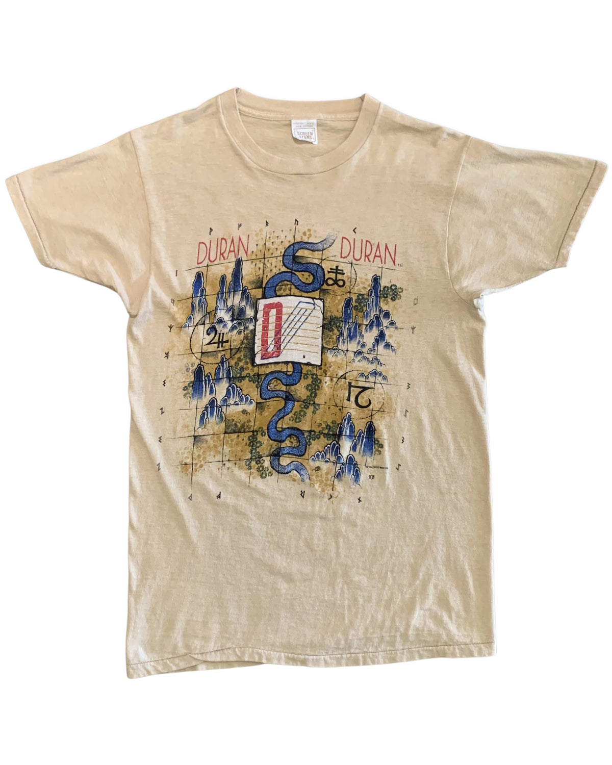 Front view of a beige Duran Duran 1984 tour T-shirt with a blue serpent, stylized mountains, numbers, symbols, and red and blue graphic details.
