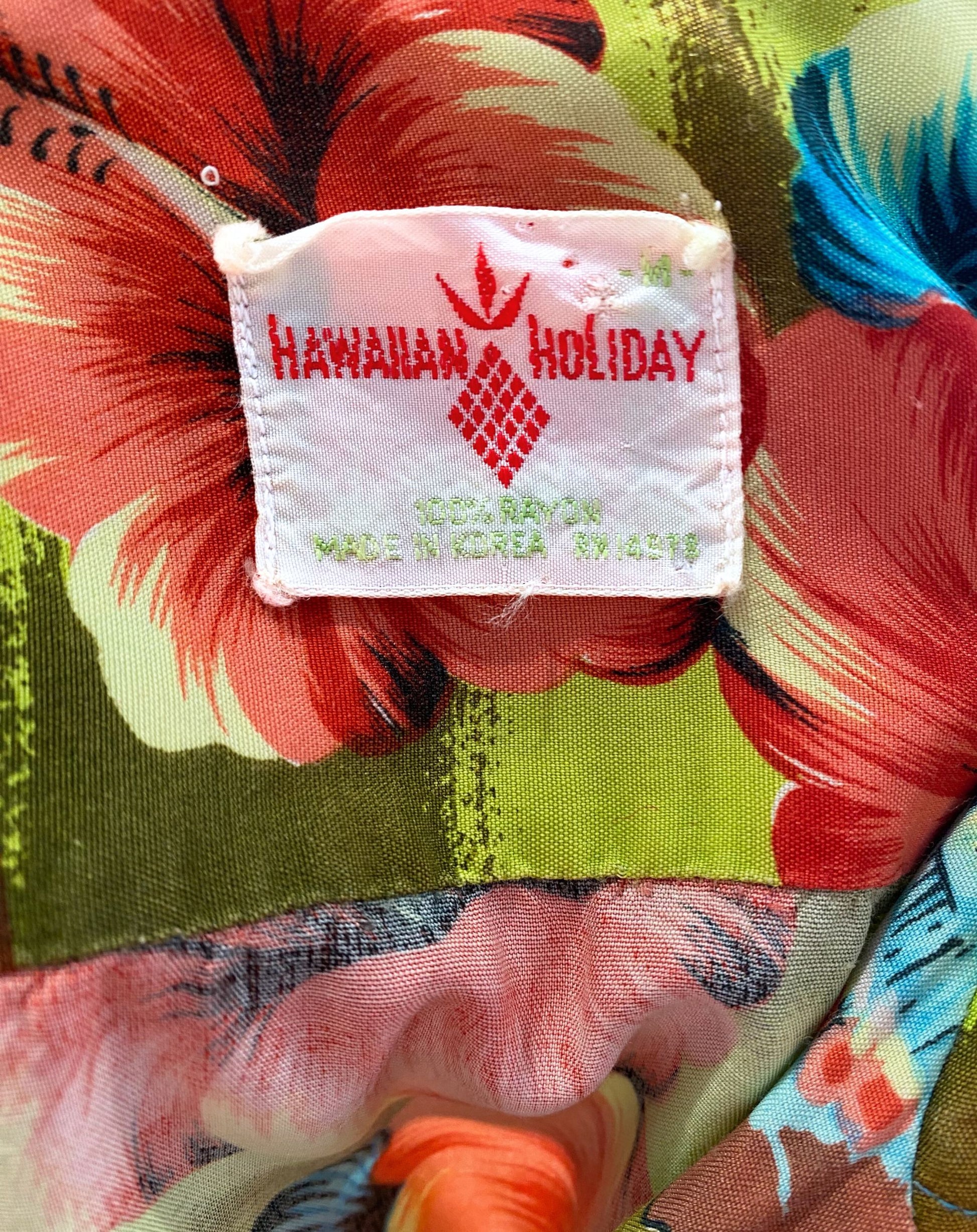 Vintage 1960s Hawaiian Holiday shirt in green, blue, and red rayon with island print. View of label.