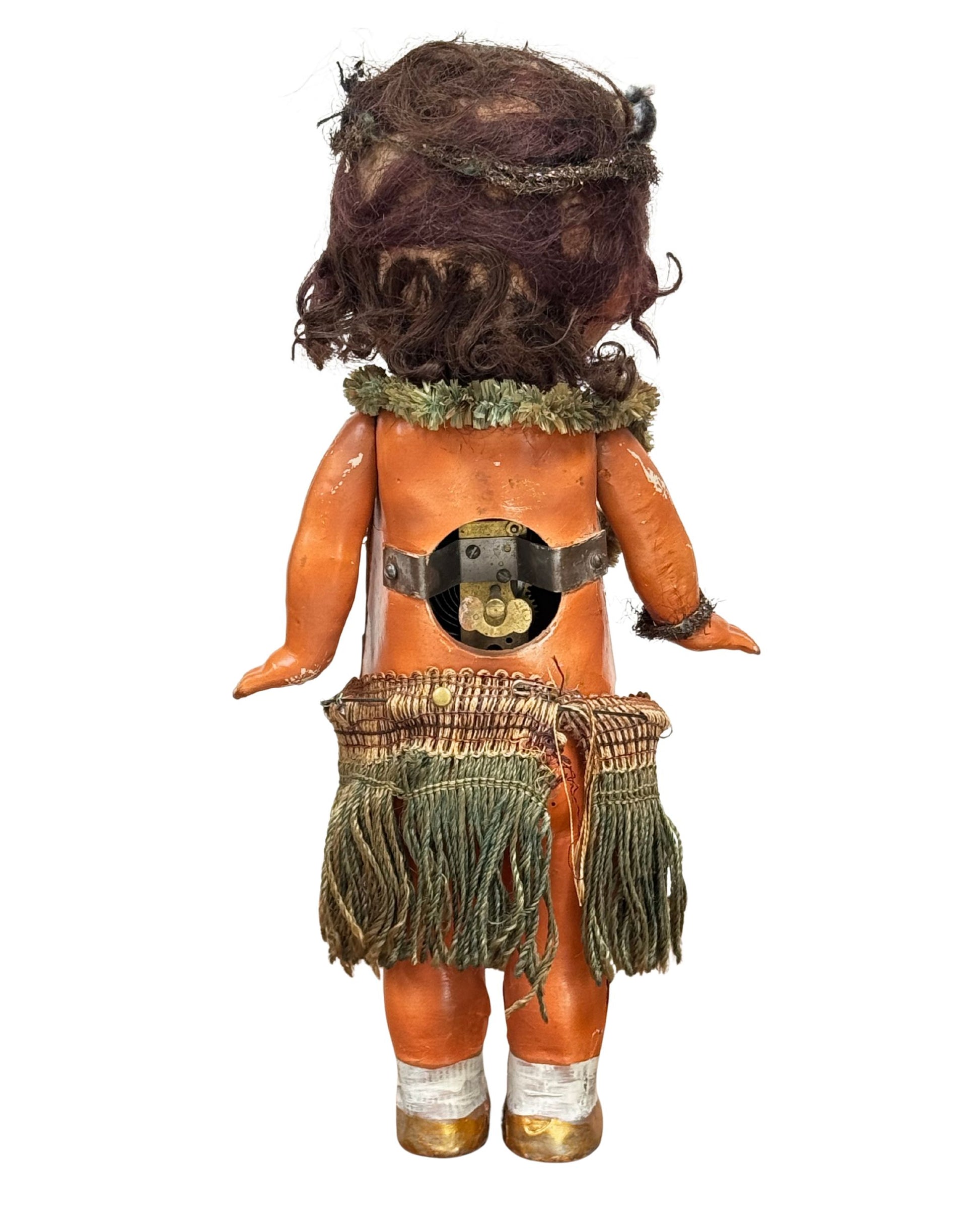Back view of 1920s mechanical hula girl doll with grass skirt, painted composition face, and wind-up movement - showing wind-up mechanism.
