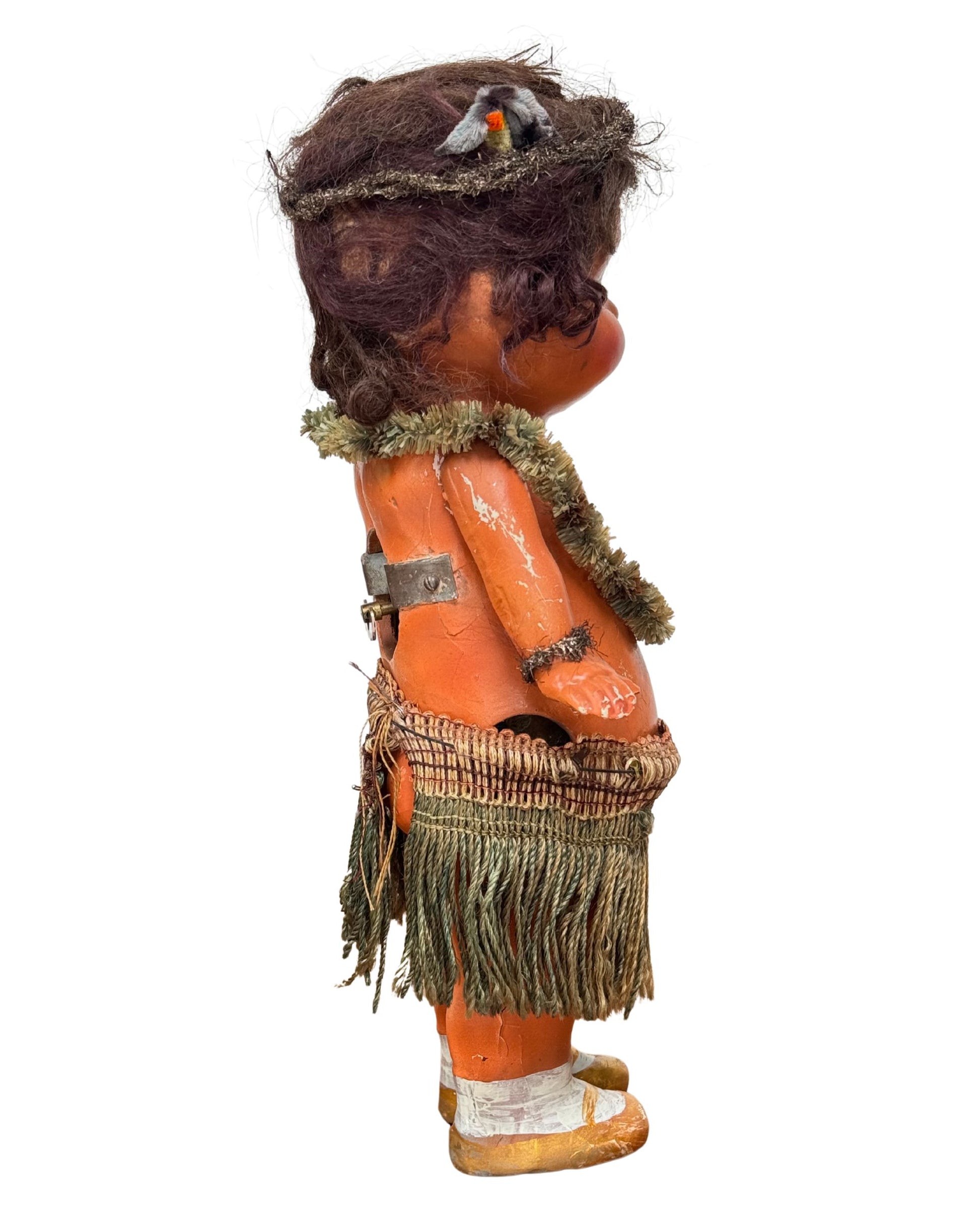 Side iew of 1920s mechanical hula girl doll with grass skirt, painted composition face, and wind-up movement.