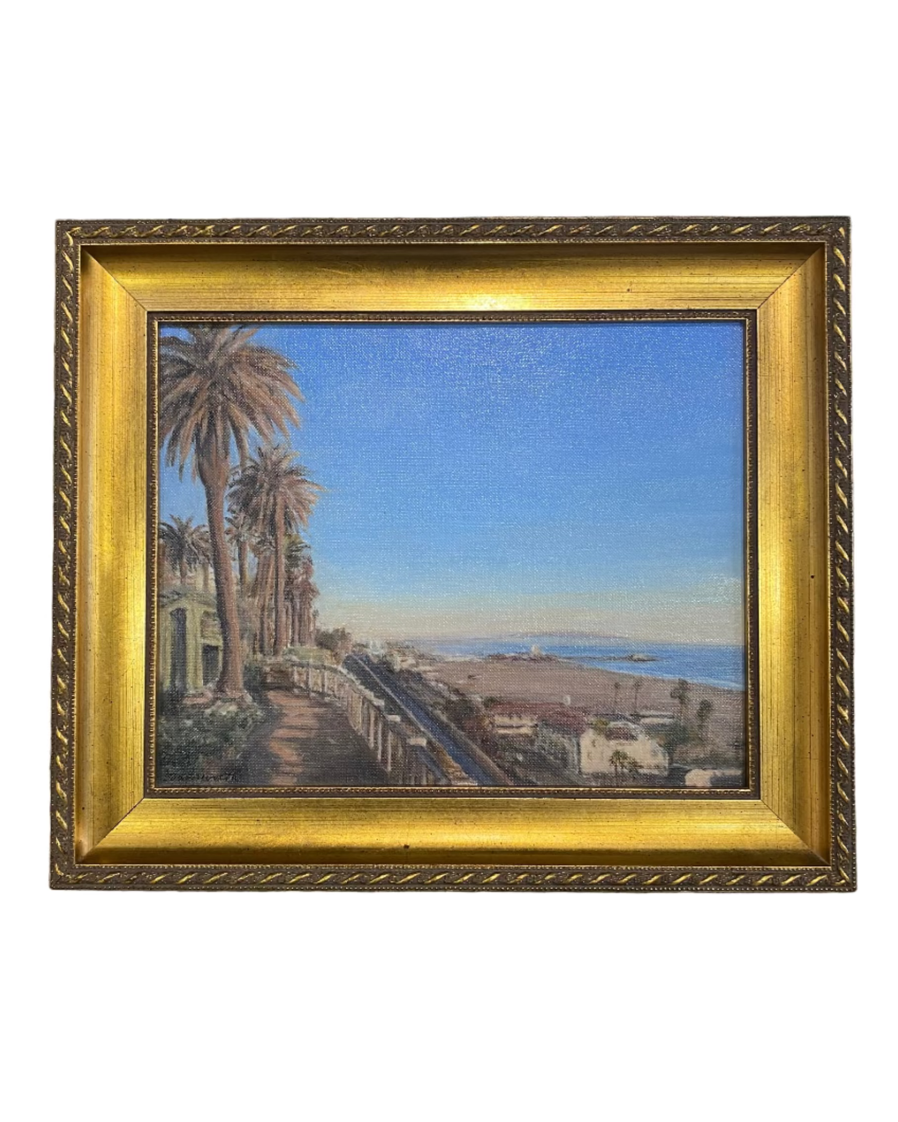 Framed painting of Santa Monica coastal scene with palm trees, blue sky and the Santa Monica Coast in gold frame. 