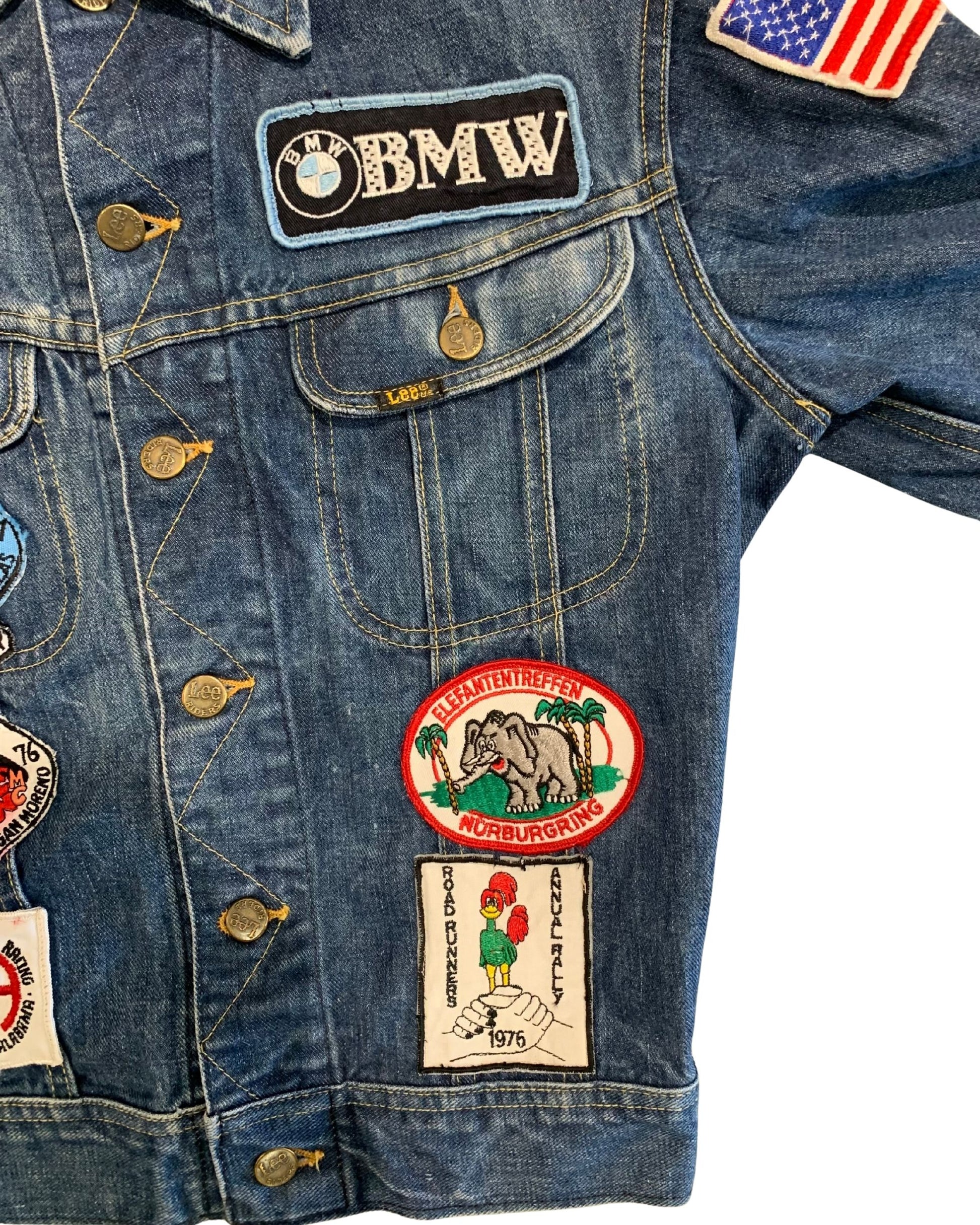 Close-up of the right front of a Lee denim jacket with a BMW patch, American flag patch, Elefantentreffen Nürburgring patch, and 1976 Road Runners rally patch.