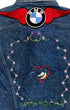 Close-up of the back of a faded denim jacket with a large red-winged BMW patch and hand-embroidered flowers surrounding a small heart motif.