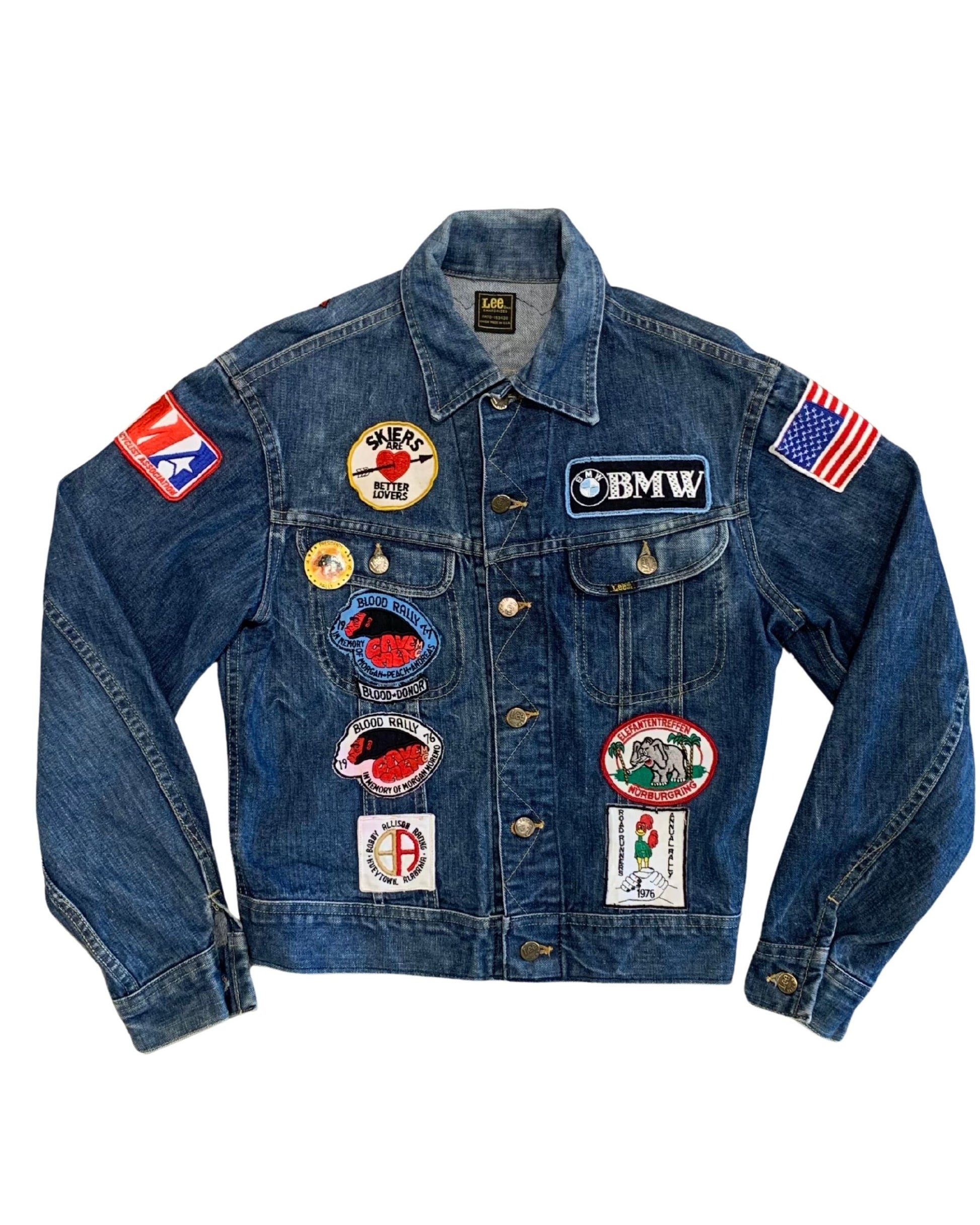 Front view of a faded blue Lee denim jacket covered with BMW, motorcycle rally, American flag, AMA, novelty patches, and vintage pins.
