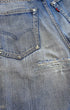 Close-up of the rear seat showing worn back pockets, faded denim, abrasions, tears, and repaired areas below the pockets.