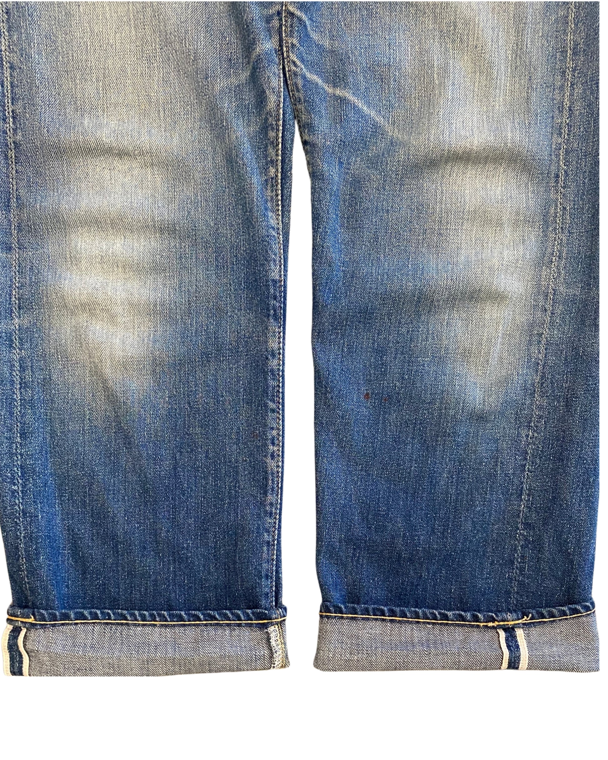 Close-up of the faded lower denim legs with rolled cuffs revealing the selvedge edges and small visible marks.