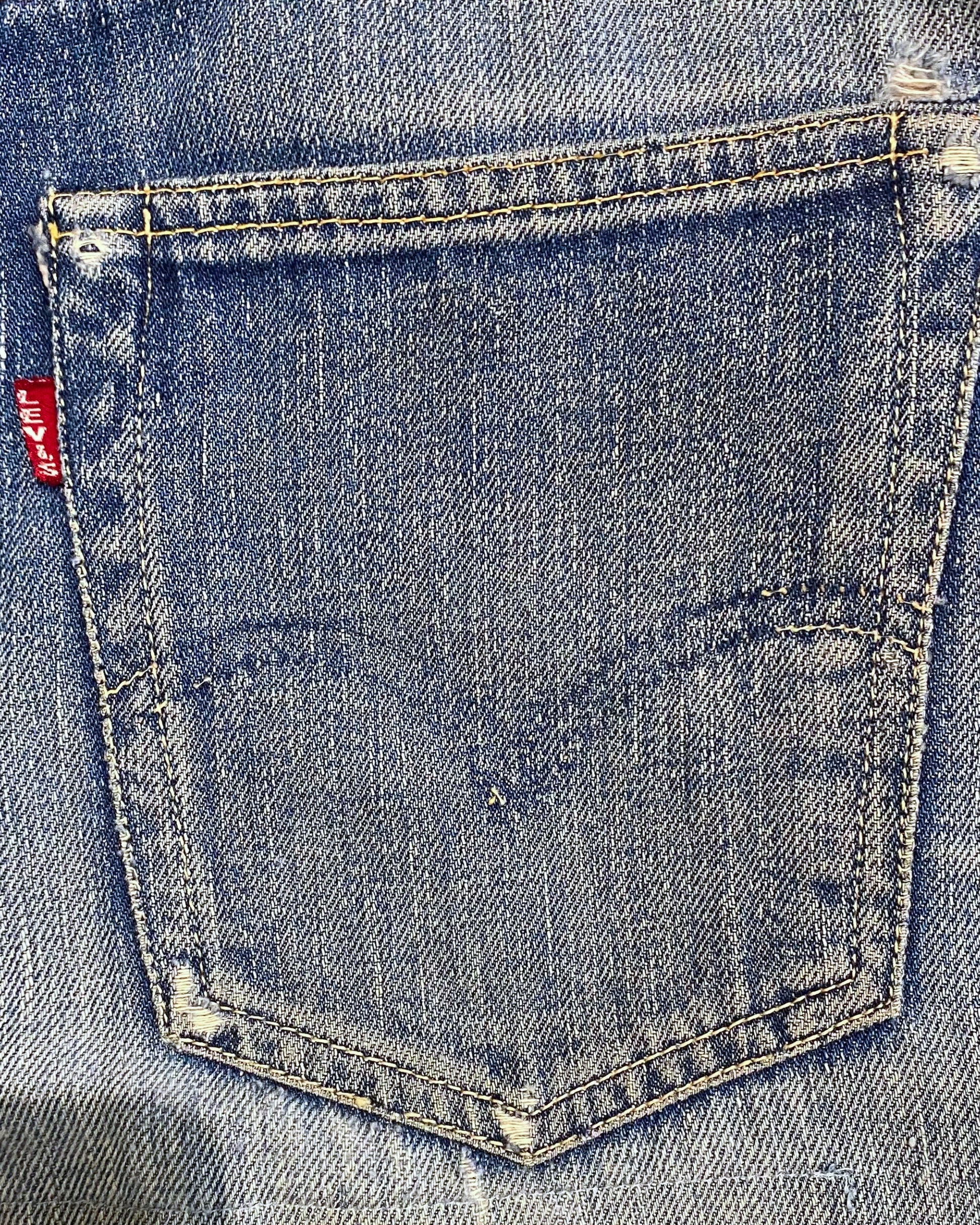Close-up of a worn Levi’s back pocket with faded arcuate stitching, frayed corners, and a red Big E tab.