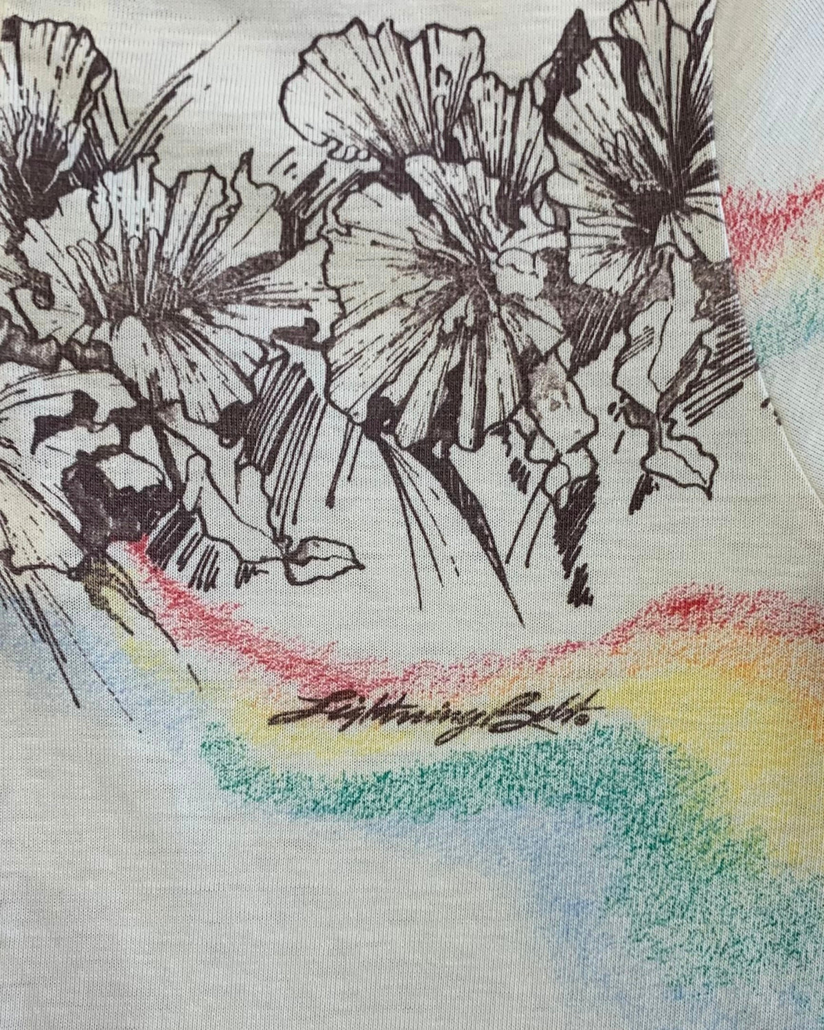 Close-up of black floral line artwork, rainbow-colored accents, and Lightning Bolt script printed on cream fabric.
