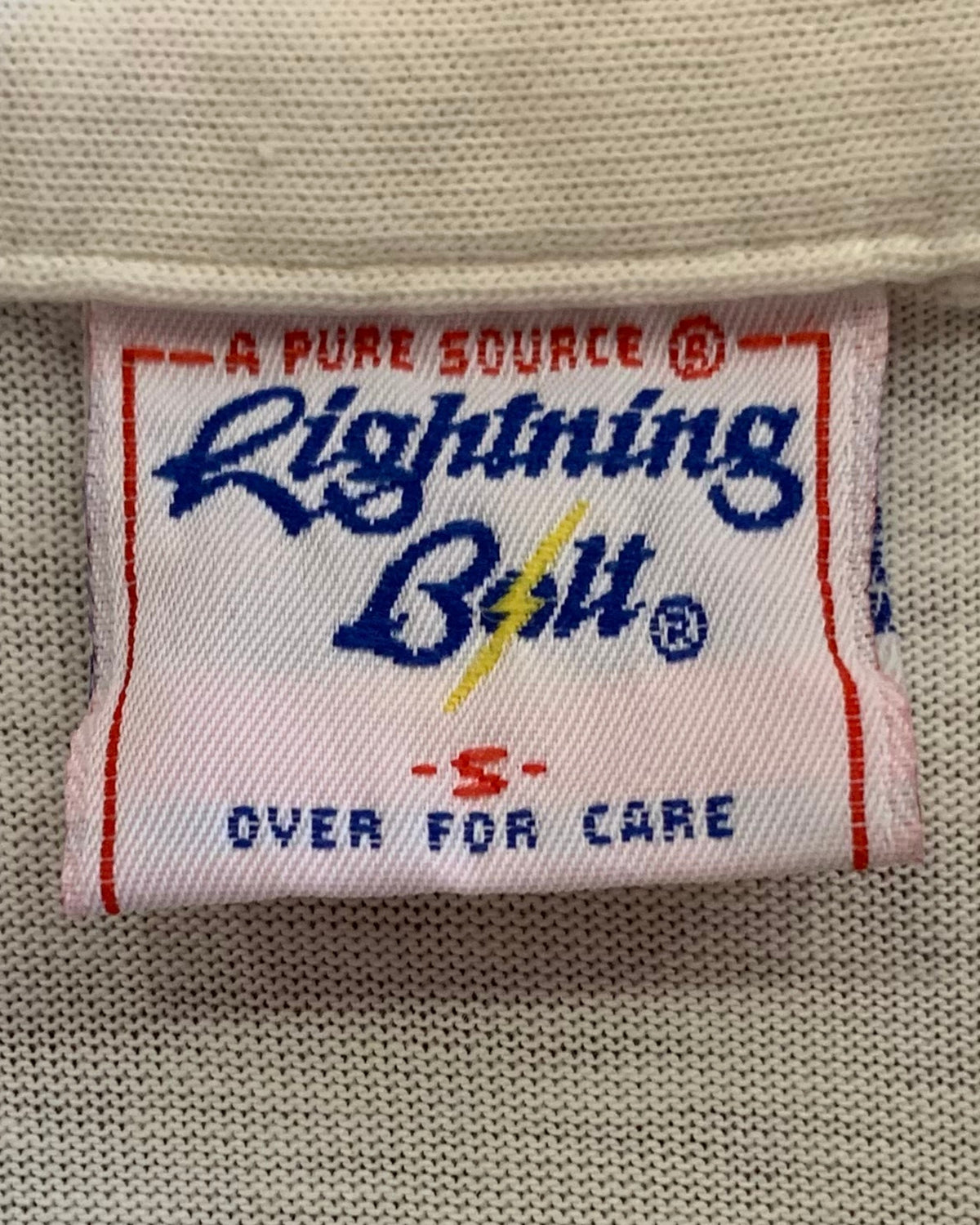 Close-up of a Lightning Bolt A Pure Source woven label marked size Small inside a cream polo shirt.
