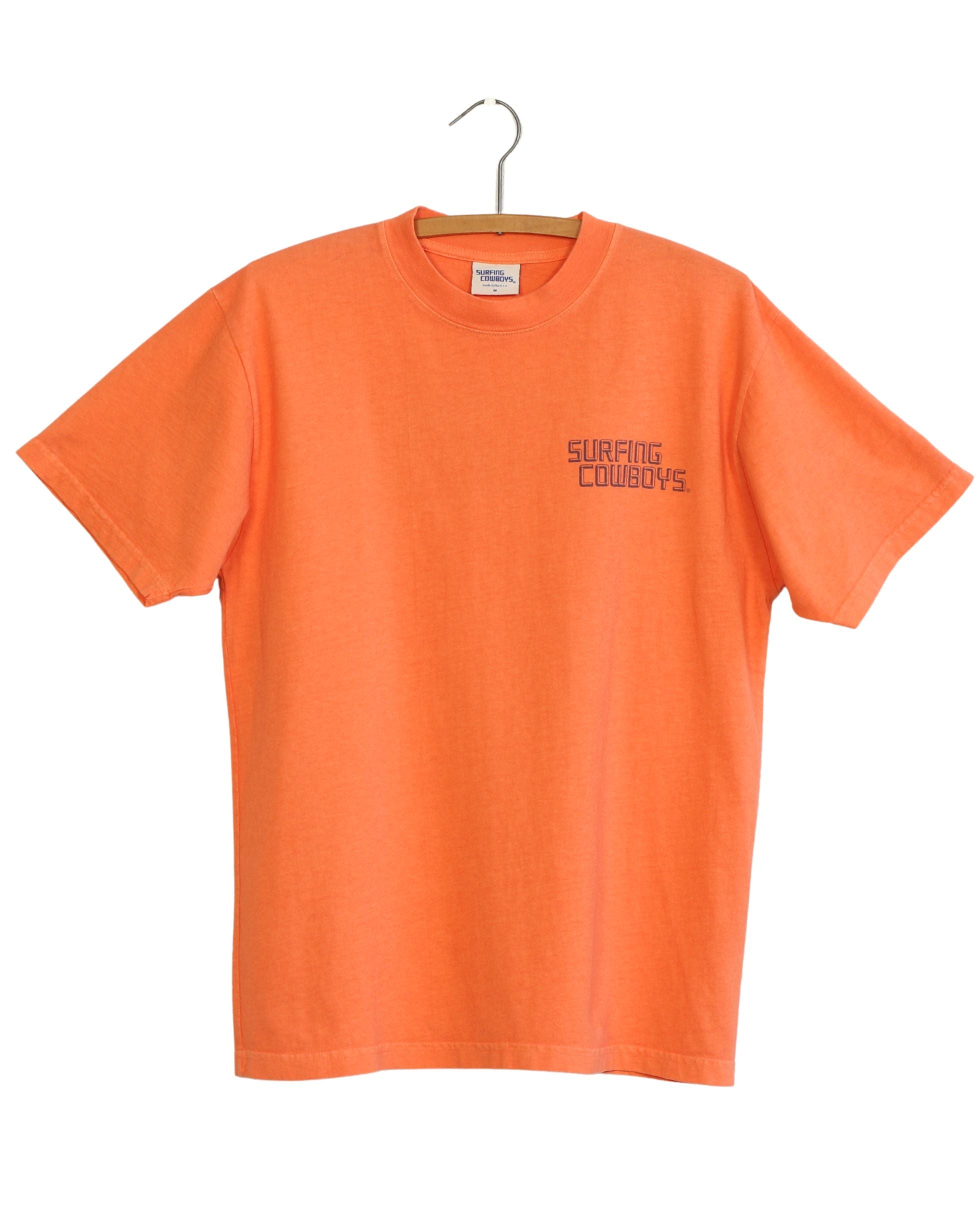 Orange t-shirt with 'Surfing Cowboys' text on a hanger against a white background