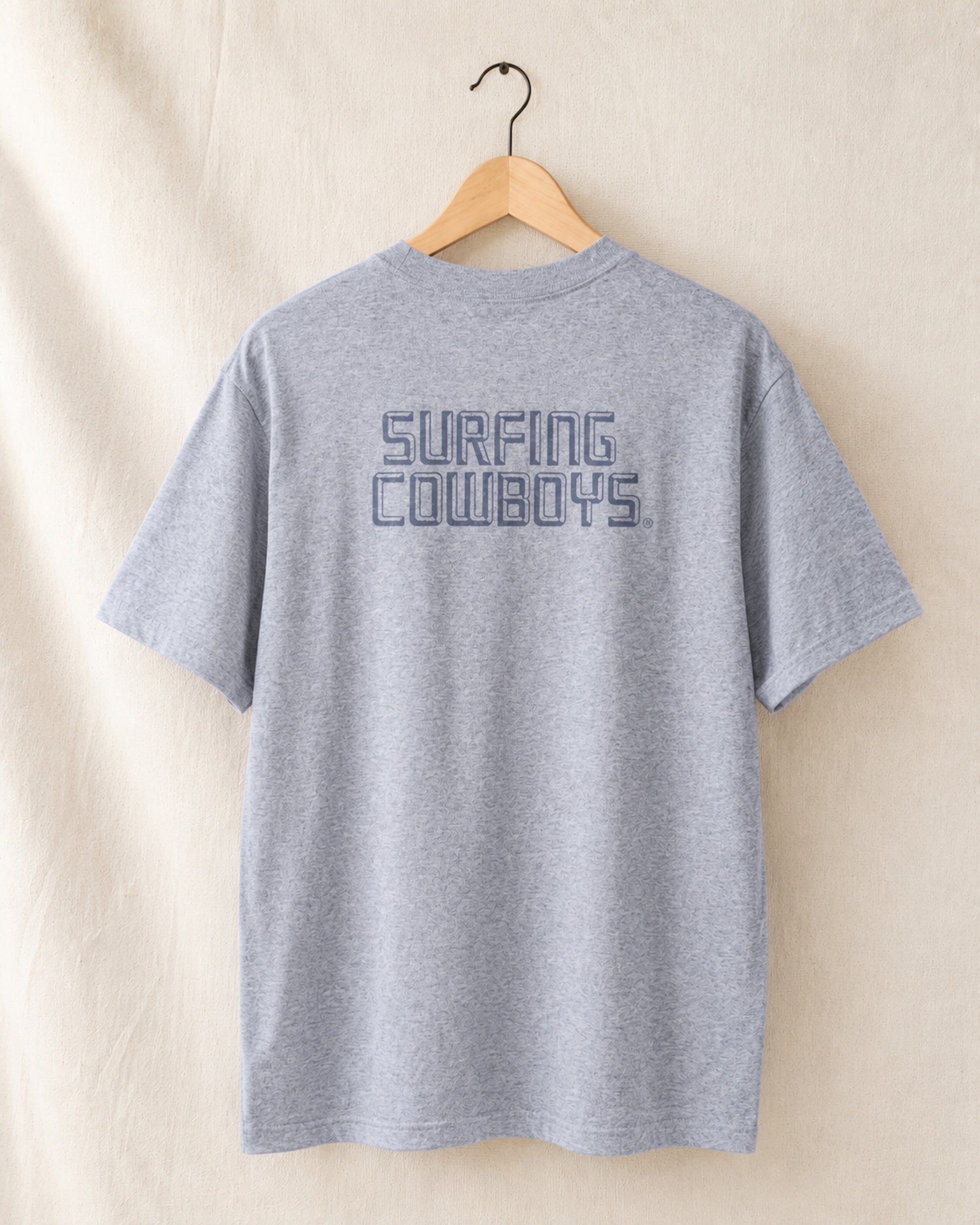 Back of Logo T in Heather Grey hanging on hanger with Surfing Cowboys Logo on center back.