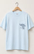 Surfing Cowboys Making Waves High Crew Pocket T-Shirt in jade blue with graphic front view on hanger.
