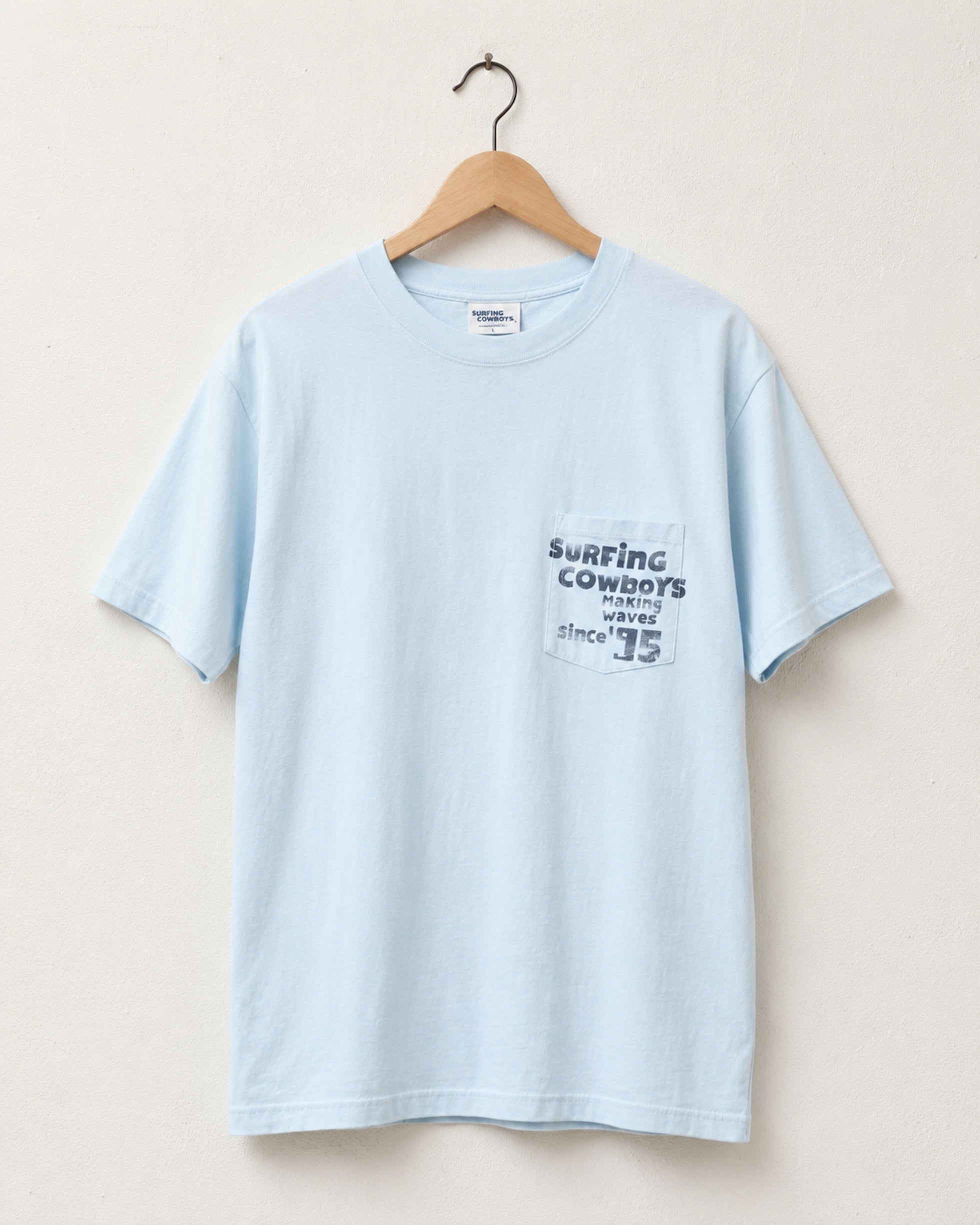 Surfing Cowboys Making Waves High Crew Pocket T-Shirt in jade blue with graphic front view on hanger.
