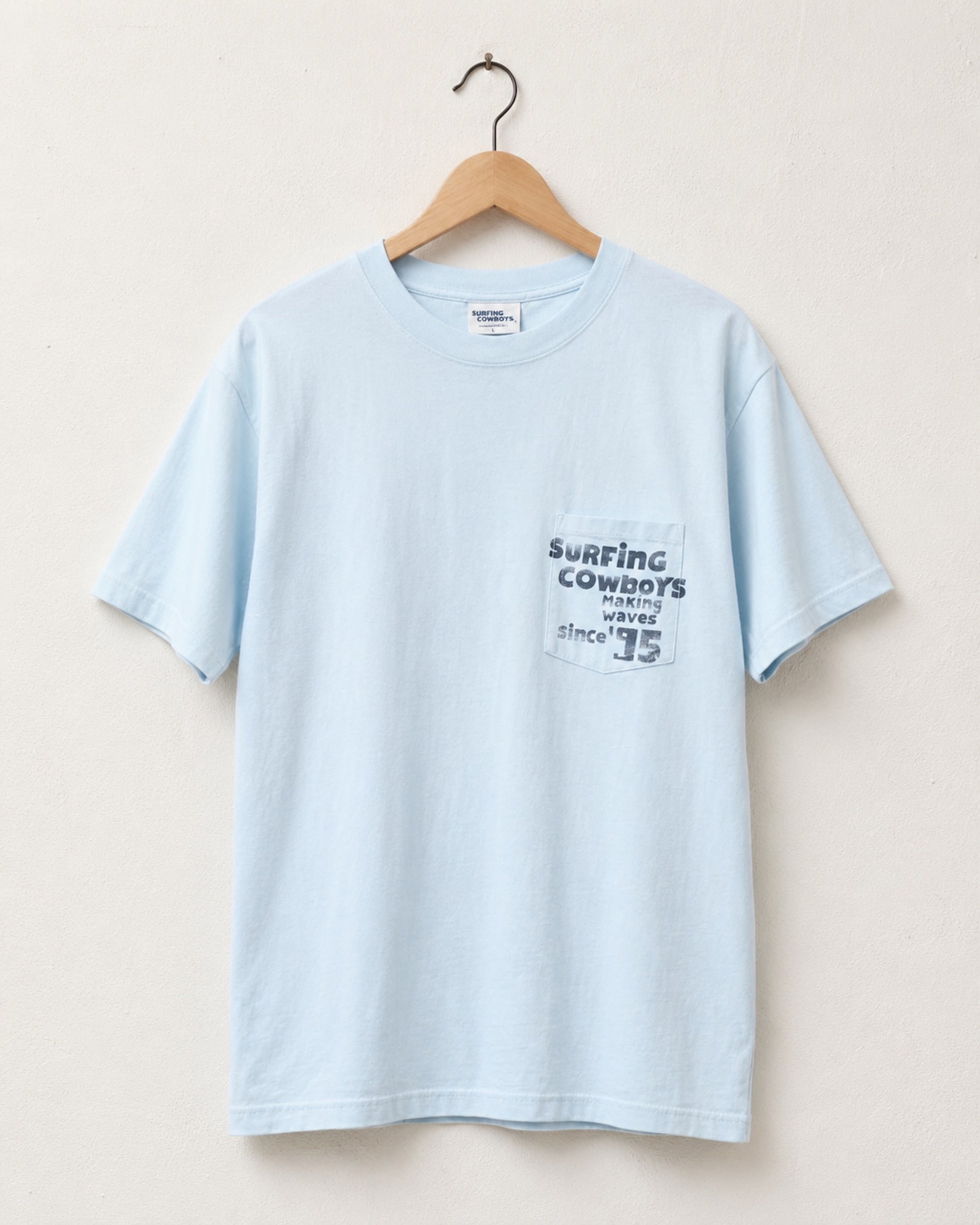 Surfing Cowboys Making Waves High Crew Pocket T-Shirt in jade blue with graphic front view on hanger.