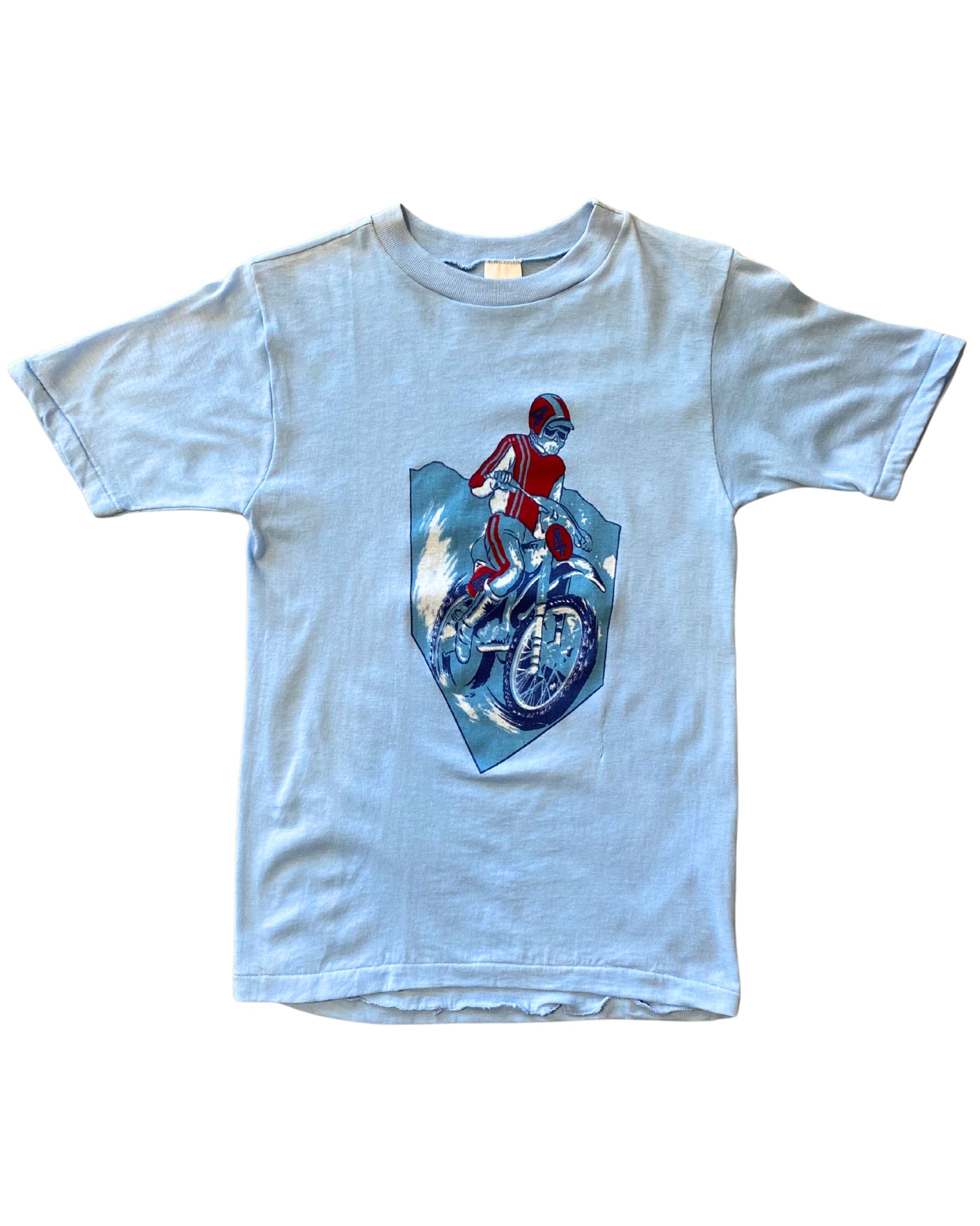 1970s youth T-shirt featuring red motorcycle rider graphic on faded blue cotton. Size 14–16. Vintage Americana style.