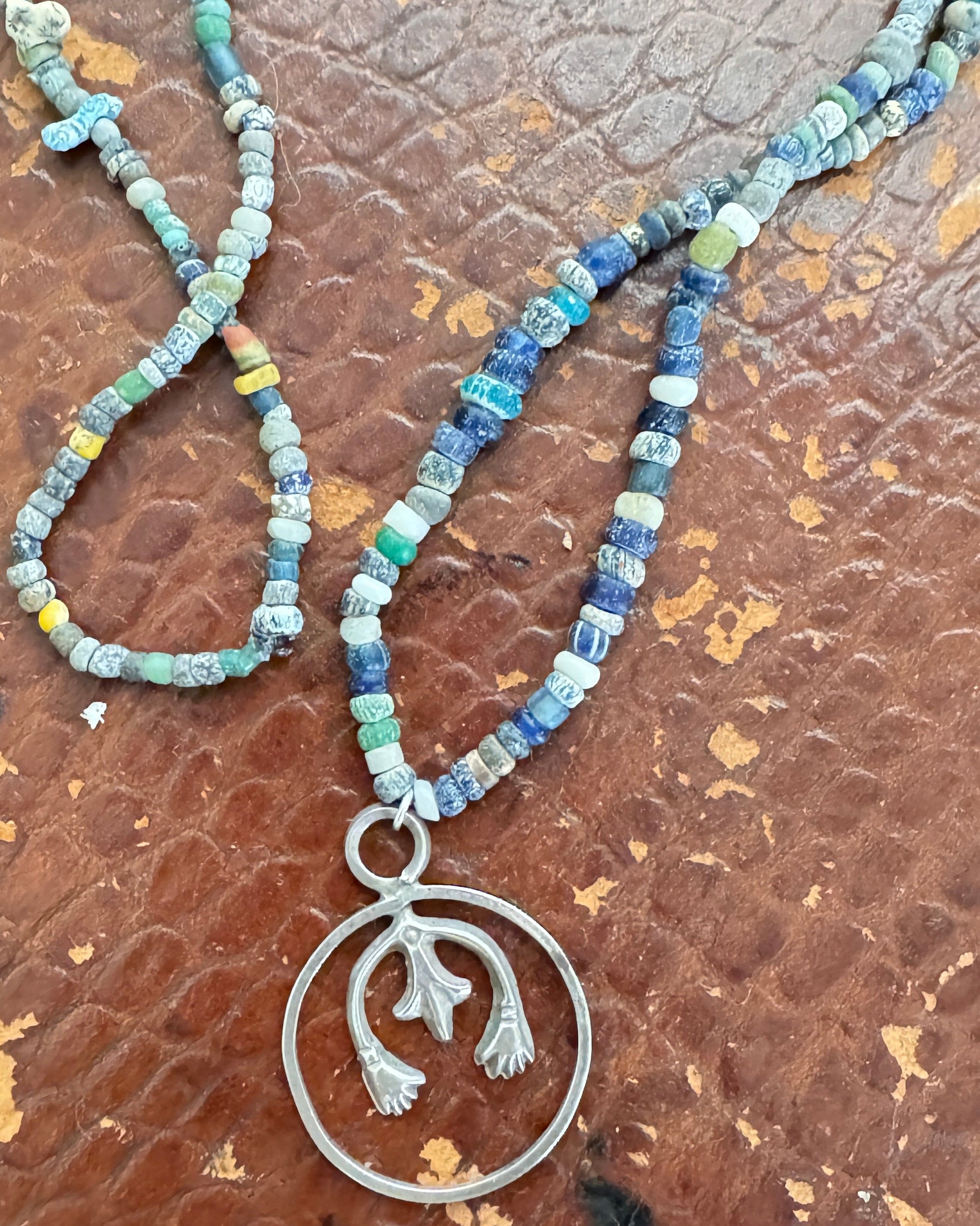Necklace with blue beads and a silver pendant on a textured brown surface