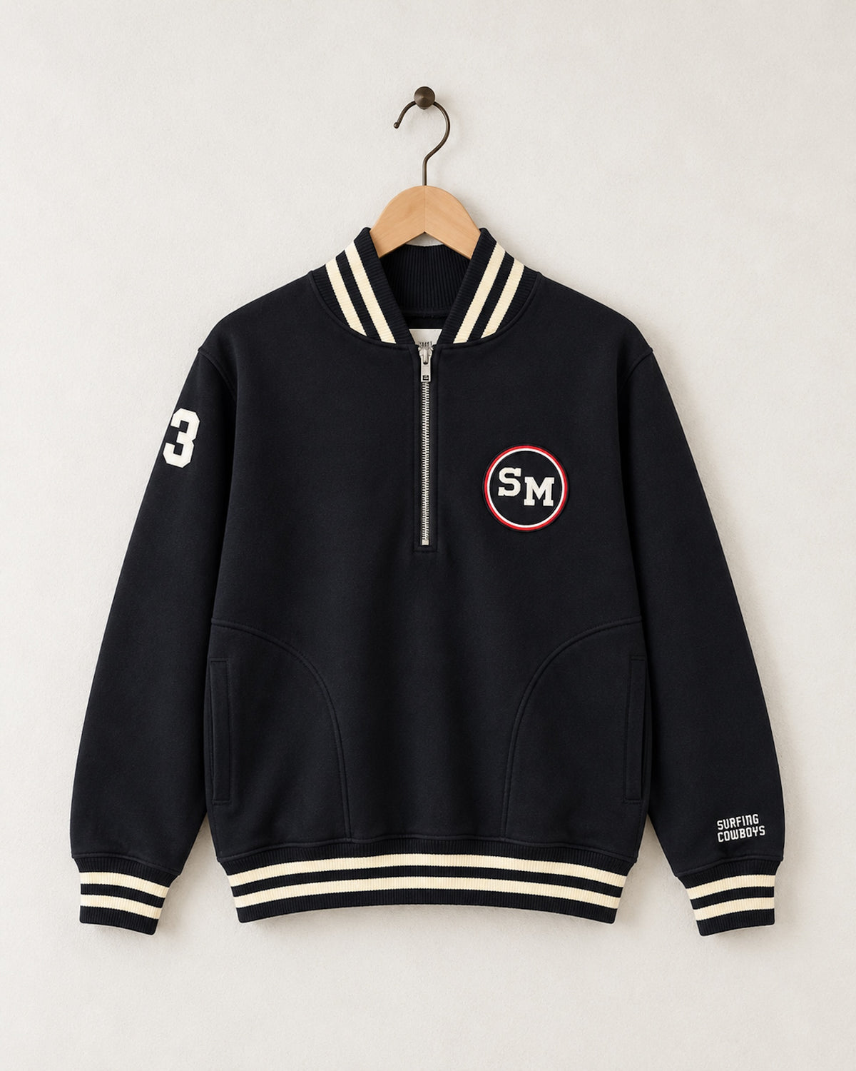 Front view of Surfing Cowboys Santa Monica Half Zip Neighborhood Sweatshirt in garment-dyed black with cream striped ribbing, red-accented SM chest patch and cream number 3 sleeve.