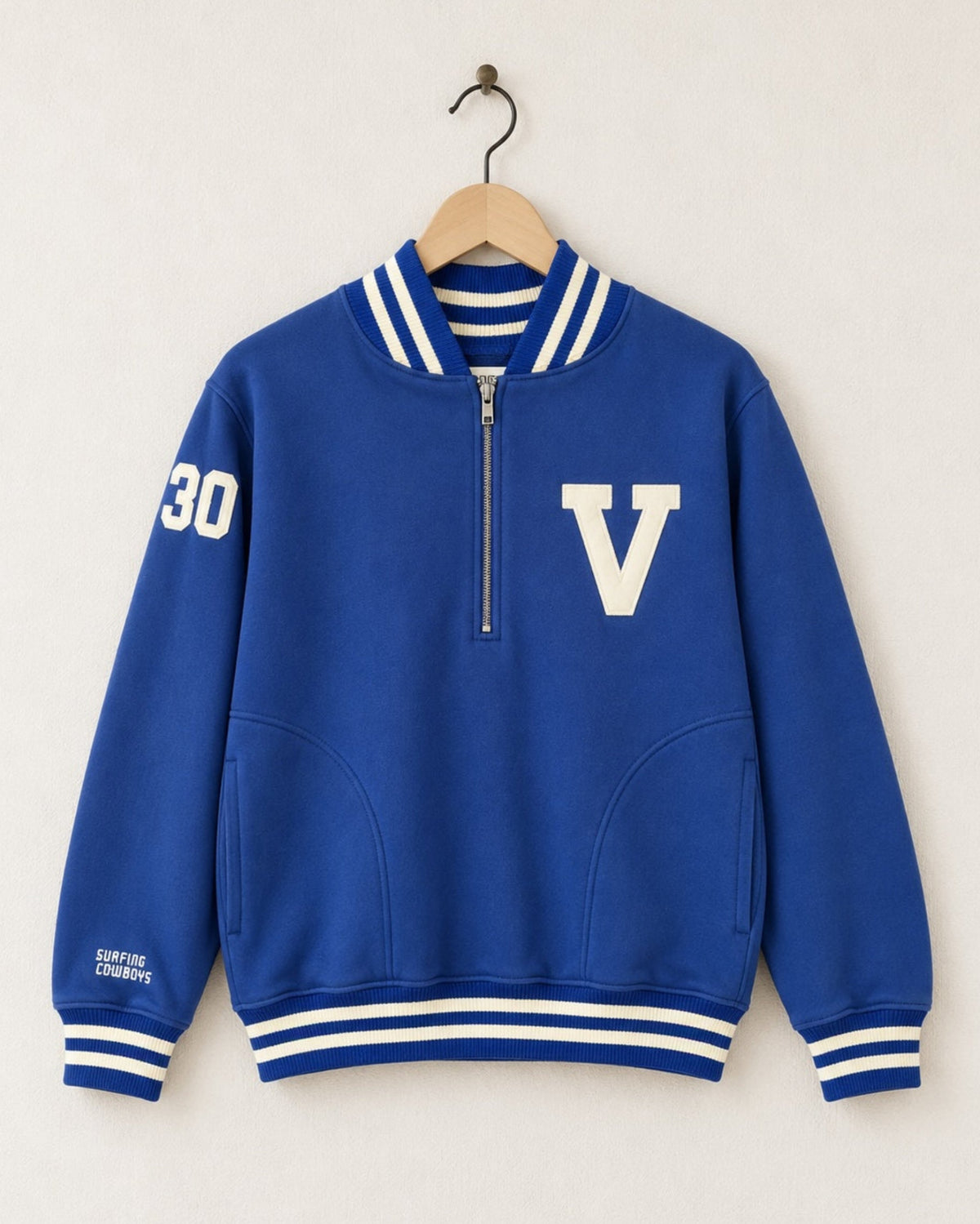 Front view of a garment-dyed Venice Blue 100% cotton half-zip sweatshirt featuring a cream varsity block letter V on the chest, striped ribbing, hand pockets, and a felt 30 patch on the sleeve.