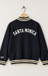 Back View of Surfing Cowboys Santa Monica Half Zip Neighborhood Sweatshirt in garment-dyed black with cream striped ribbing, Santa Monica Lettering on the back and Surfing Cowboys embroidered on the sleeve.